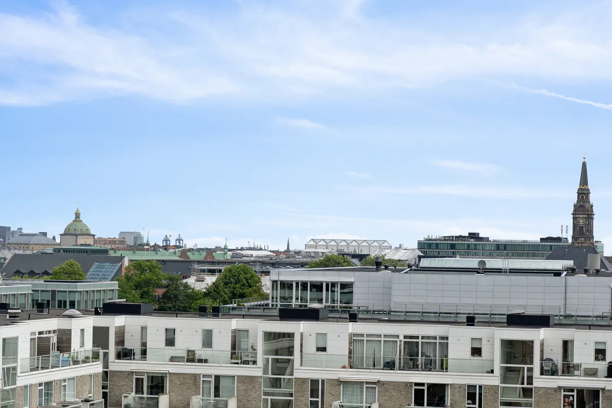 Rå og charmerende kontorlejemål med udsigt over Njalsgade-kvarterets bygninger, glasruder og spiret fra St. Knuds Kirke i baggrunden. Forskellige bygninger og træer.