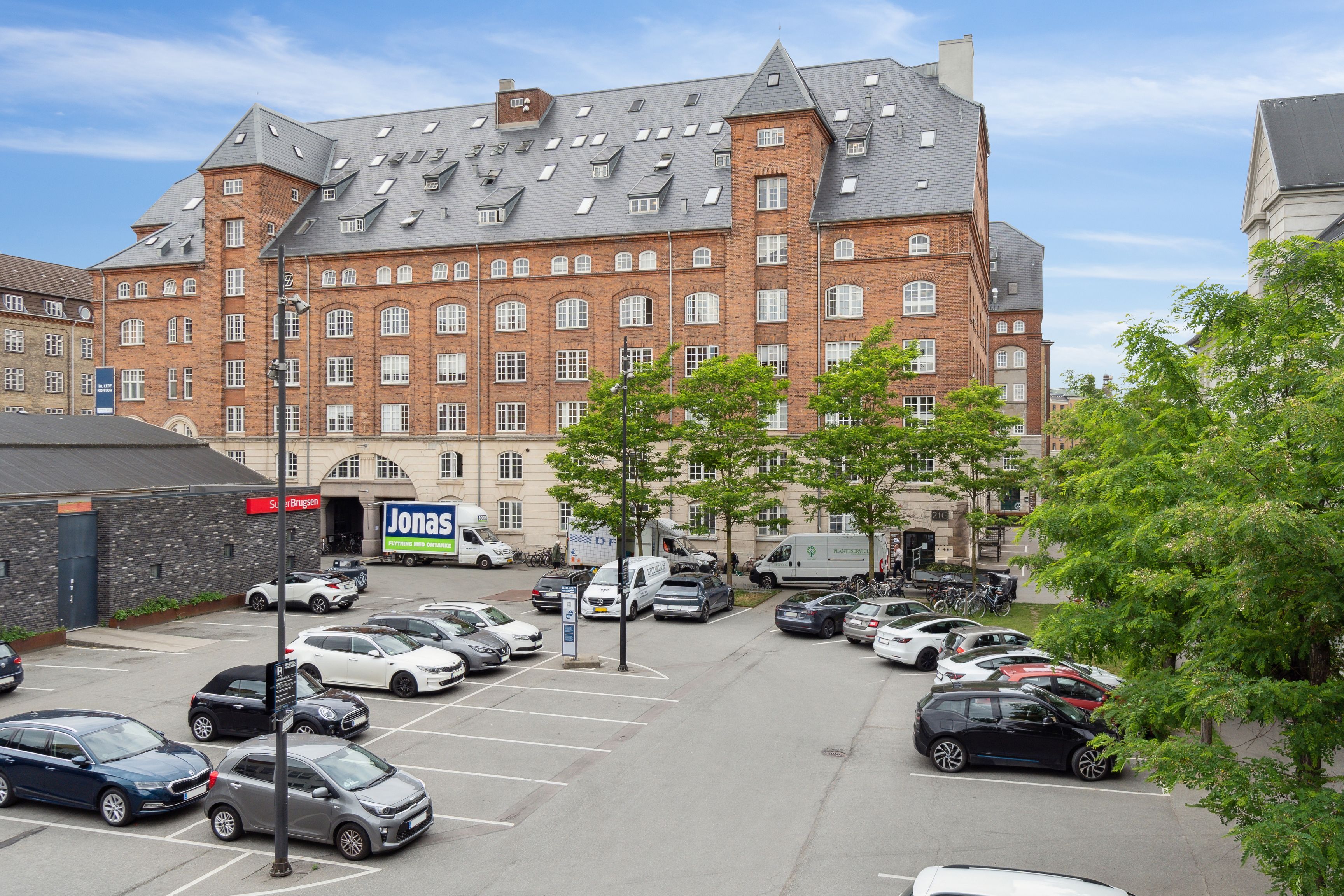 Kontorlejemål med rå detaljer og kreativ atmosfære til leje i Njalsgade 21G, 8., 2300 København S. Parkeringsplads med flere biler og Jonas-reklameskilt.