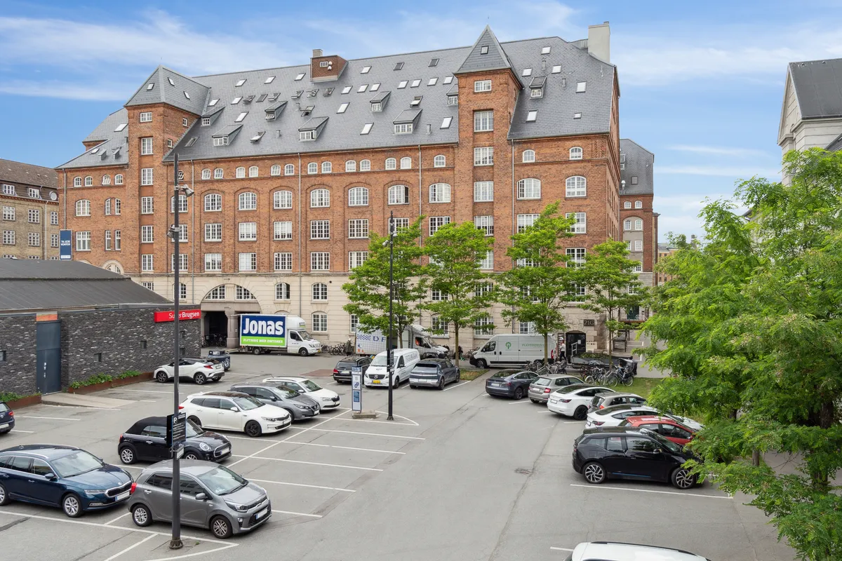 Kontorlejemål med rå detaljer og kreativ atmosfære til leje i Njalsgade 21G, 8., 2300 København S. Parkeringsplads med flere biler og Jonas-reklameskilt.