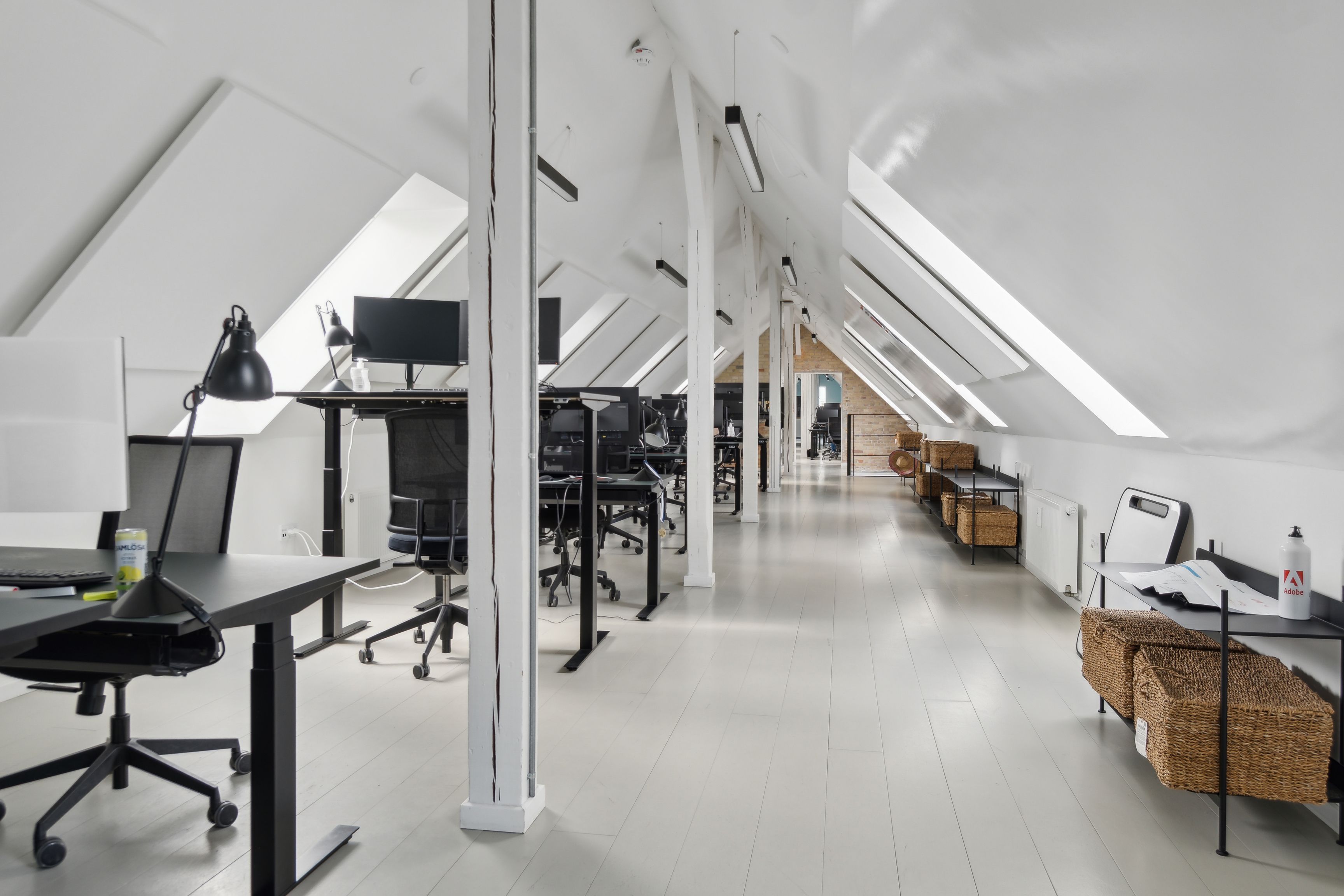 Et moderne kontorlokale med hvide vægge og loft, skriveborde og stolpe, lysekroner og vinduer med udsigt til byen