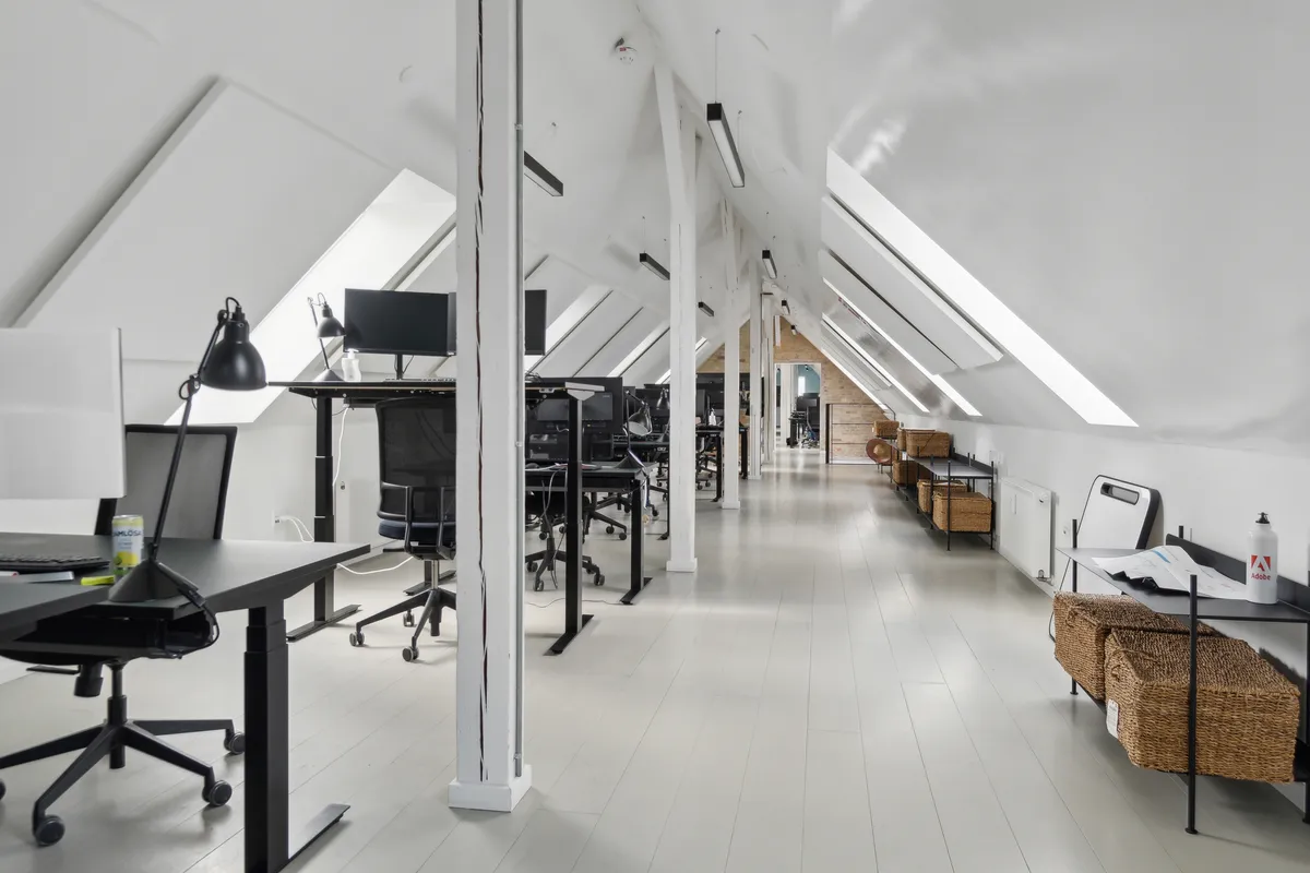 Et moderne kontorlokale med hvide vægge og loft, skriveborde og stolpe, lysekroner og vinduer med udsigt til byen