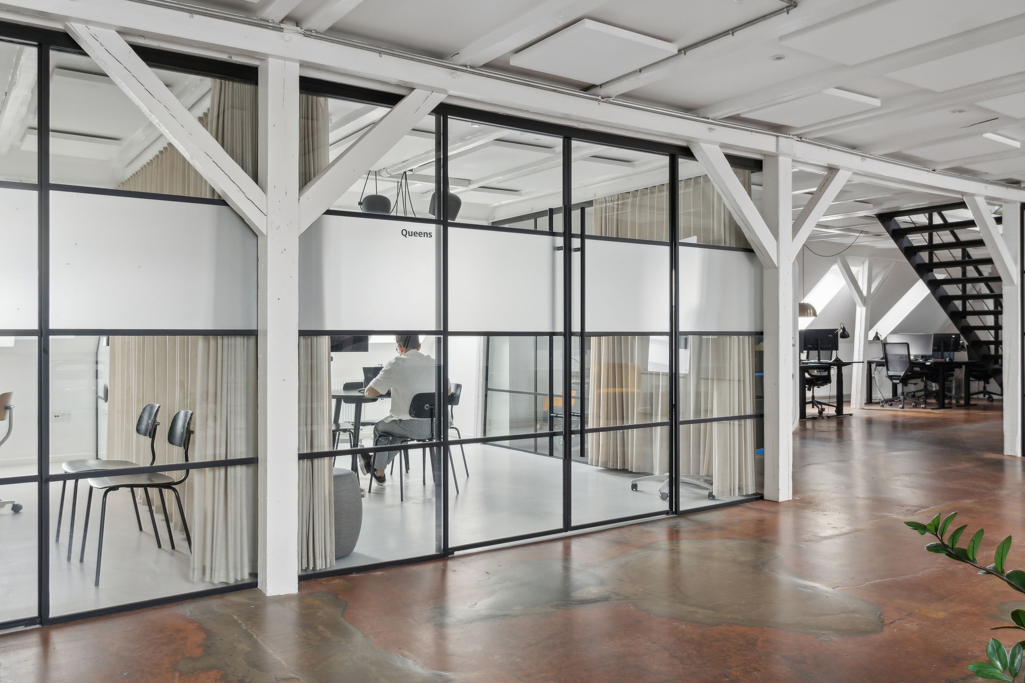 Kontor med glasvægge og lyse lofter i Njalsgade-kvarteret. En mand sidder ved et bord med computer. Rå og kreativ atmosfære med højde og bjælker.