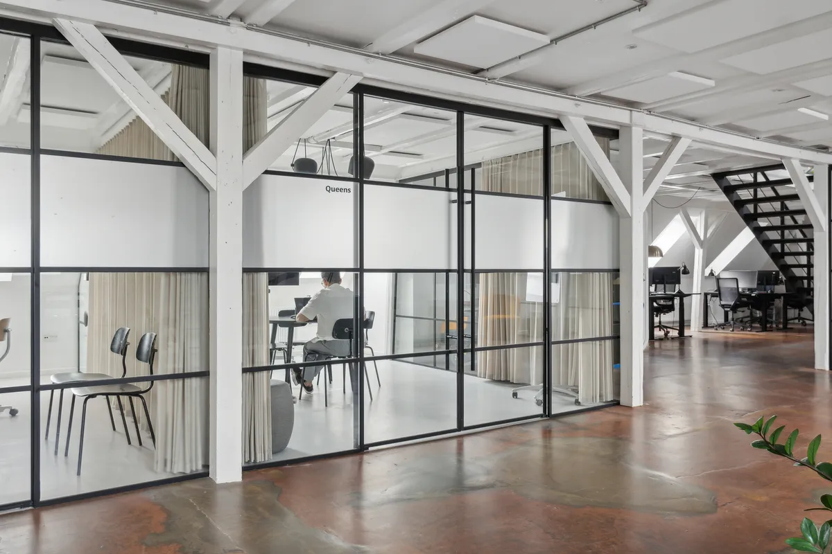 Kontor med glasvægge og lyse lofter i Njalsgade-kvarteret. En mand sidder ved et bord med computer. Rå og kreativ atmosfære med højde og bjælker.