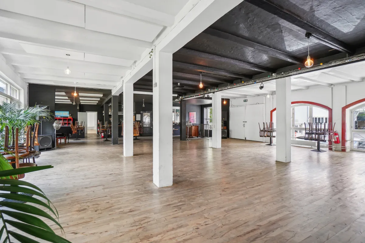 Store rum med lyse lofter og gulvtæpper. Væggene er sorte og hvide med lysepunkter. Møbler er opstillet langs væggene og på gulvet. Køkken og toilet er i baggrunden.