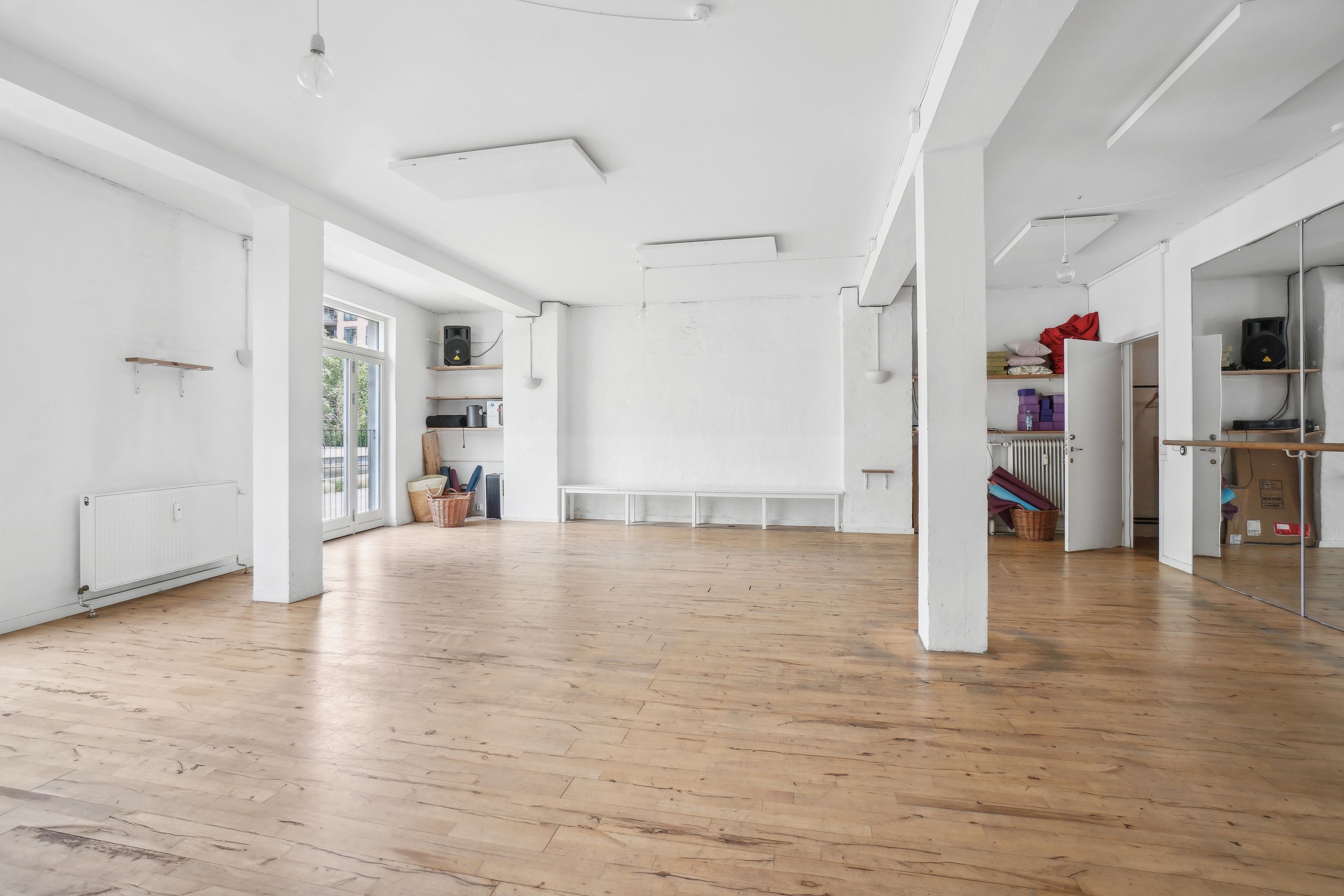 Stor og rummelig lejemål i lysefarvede lokaler med trægulv. Væggene er hvide og der er en hvid bænk langs væggen. Lokalet er fuld af lys og har store ruder.