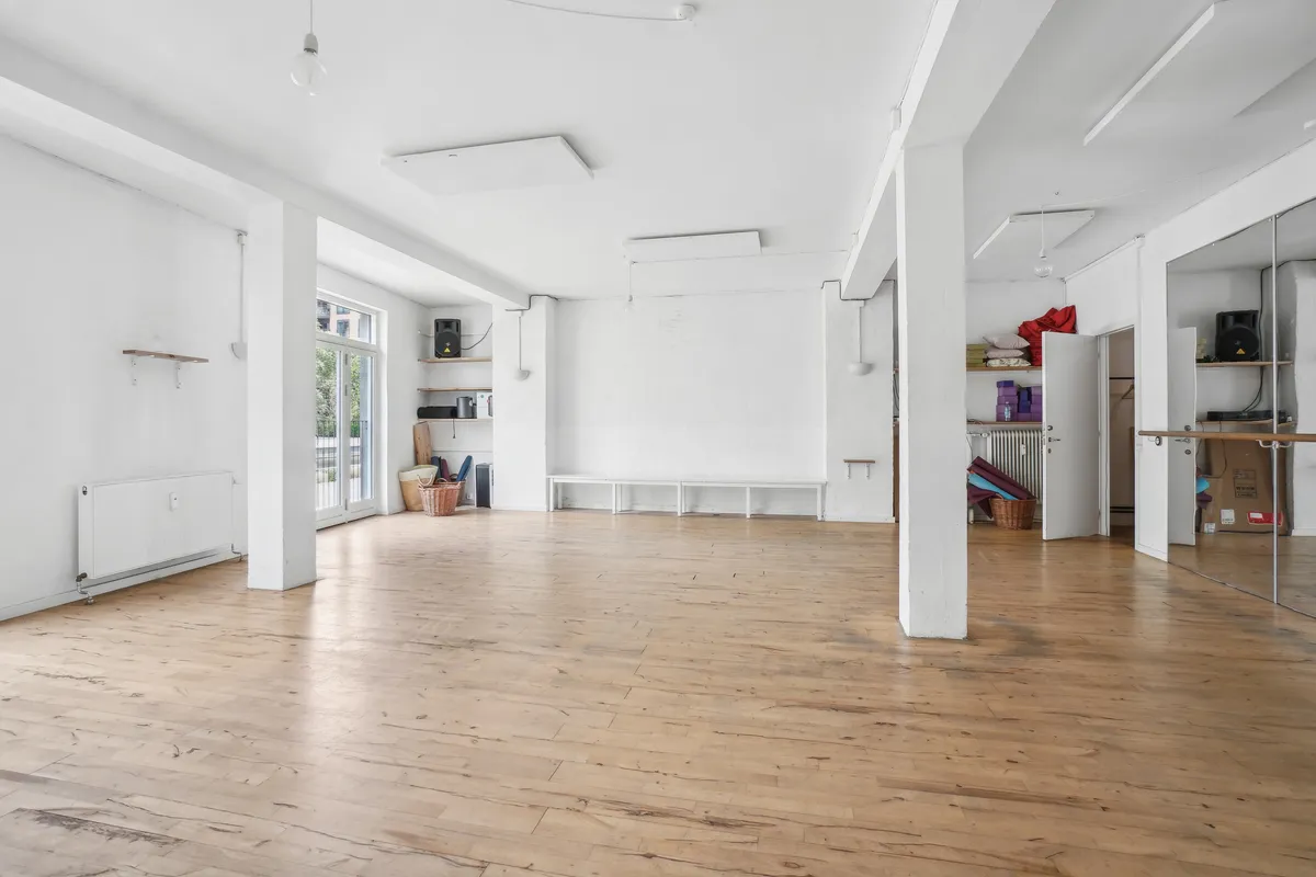 Stor og rummelig lejemål i lysefarvede lokaler med trægulv. Væggene er hvide og der er en hvid bænk langs væggen. Lokalet er fuld af lys og har store ruder.