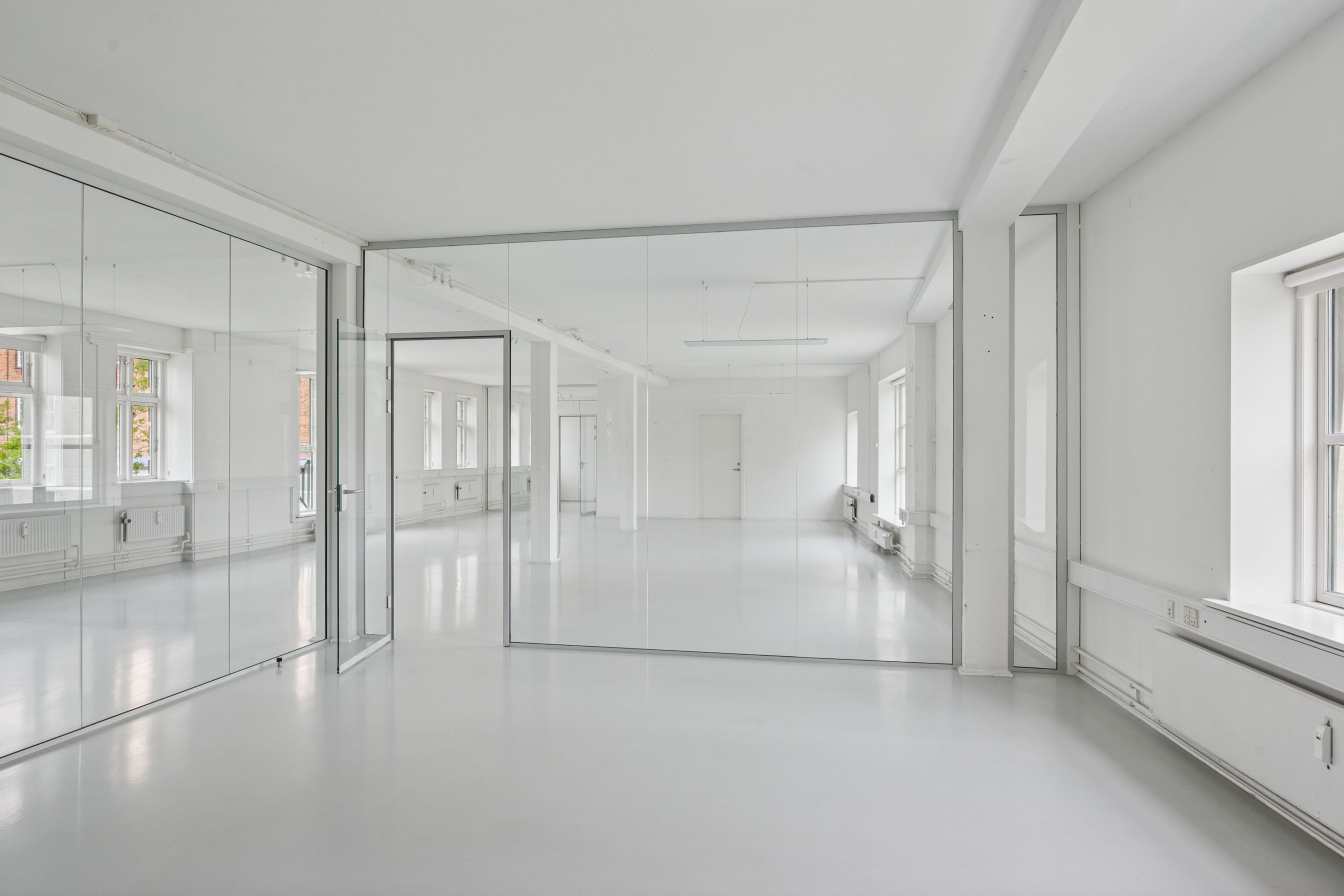 Lyst og nyt kontor med hvide vægge og gulve, store spejlglas og åbne døre til andre værelser, lyse vinduer med smukke udsigt til gaden