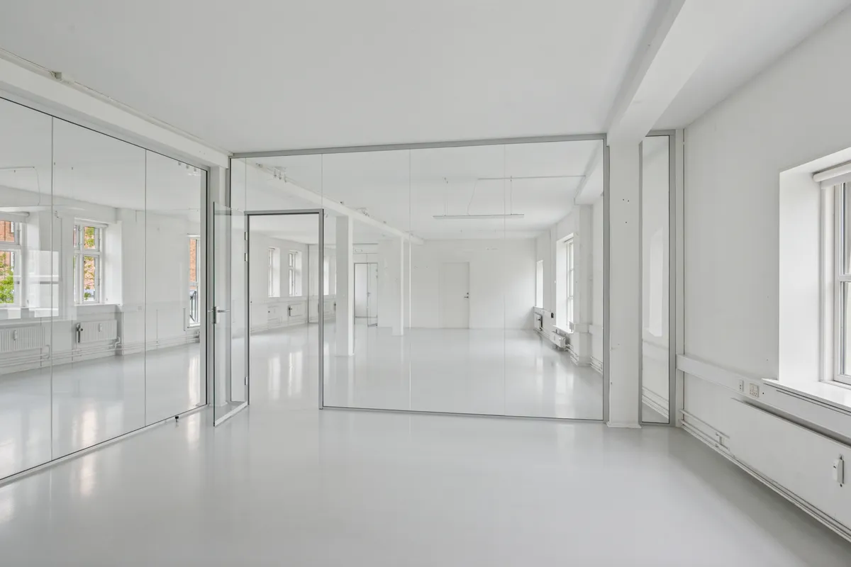 Lyst og nyt kontor med hvide vægge og gulve, store spejlglas og åbne døre til andre værelser, lyse vinduer med smukke udsigt til gaden