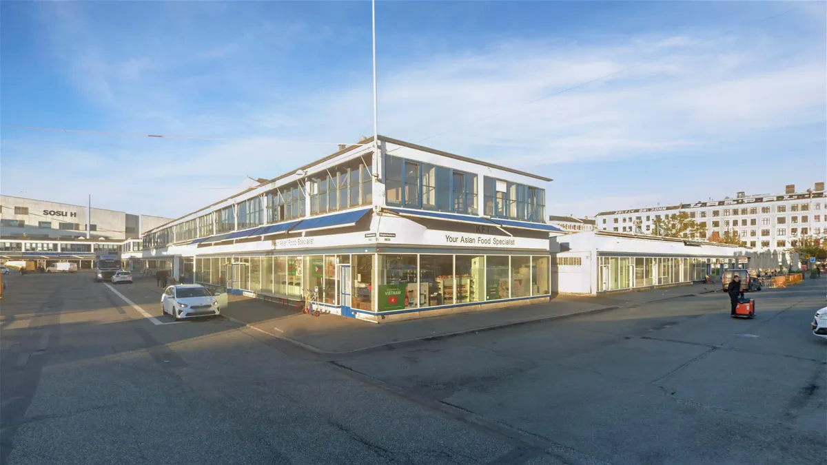 En stor bygning med teksten Your Asian Food Specialist står på hjørnet af en tomtom, hvor en bil er parkeret