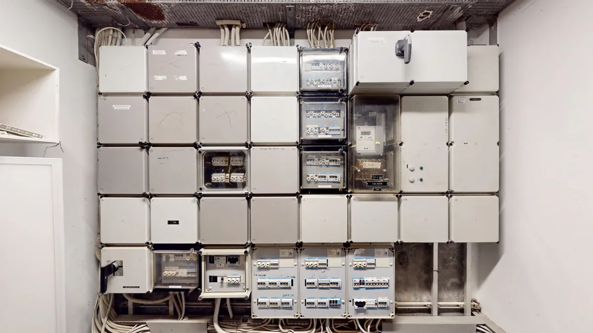 Et stort antal hvide elektriske skabe står i en række i en rummelig lokale med mange ledninger