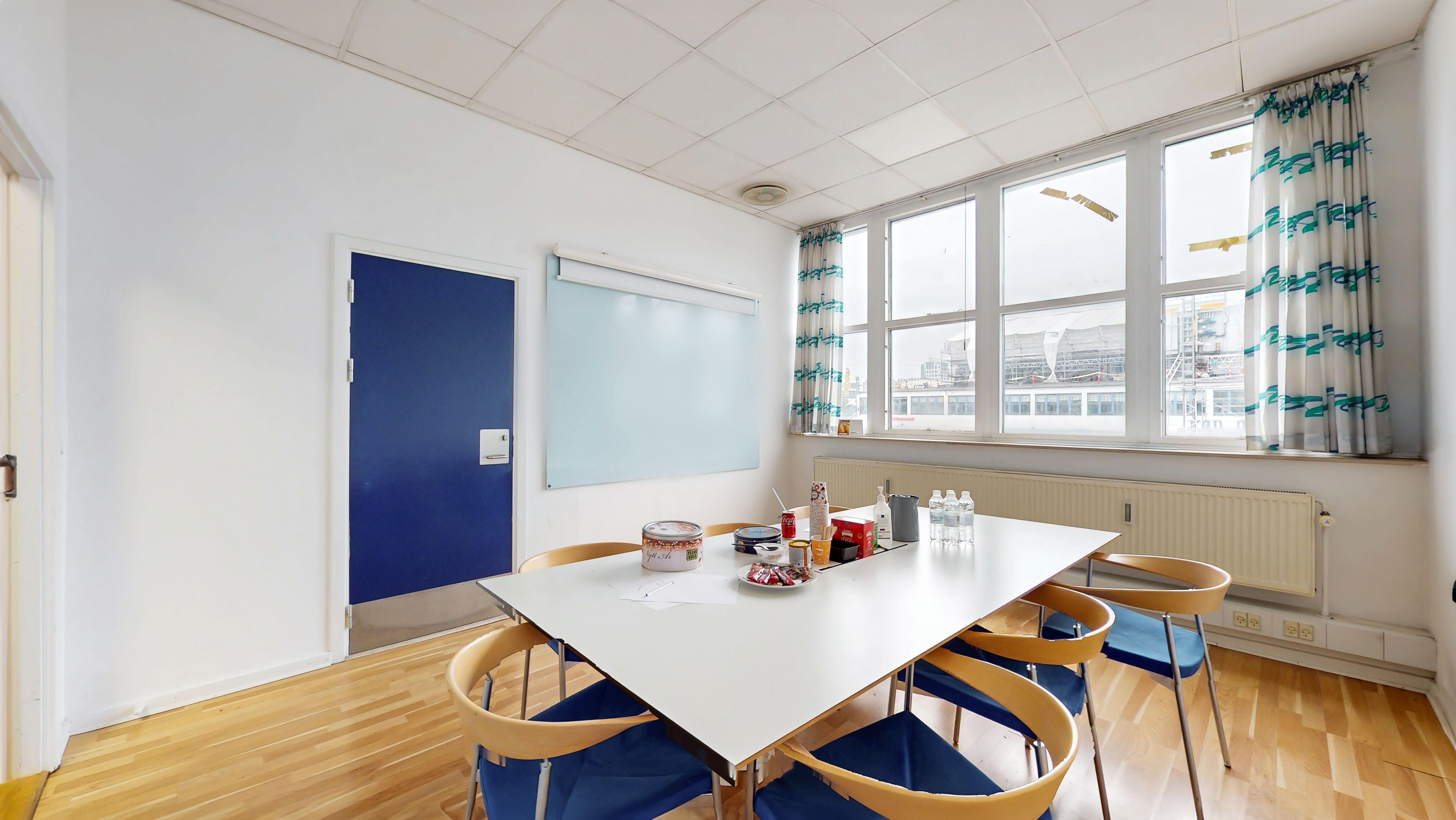 Hvidt mødelokale med ovalt bord og fem lysestole samt en dør og et vindue med udsigt over byen