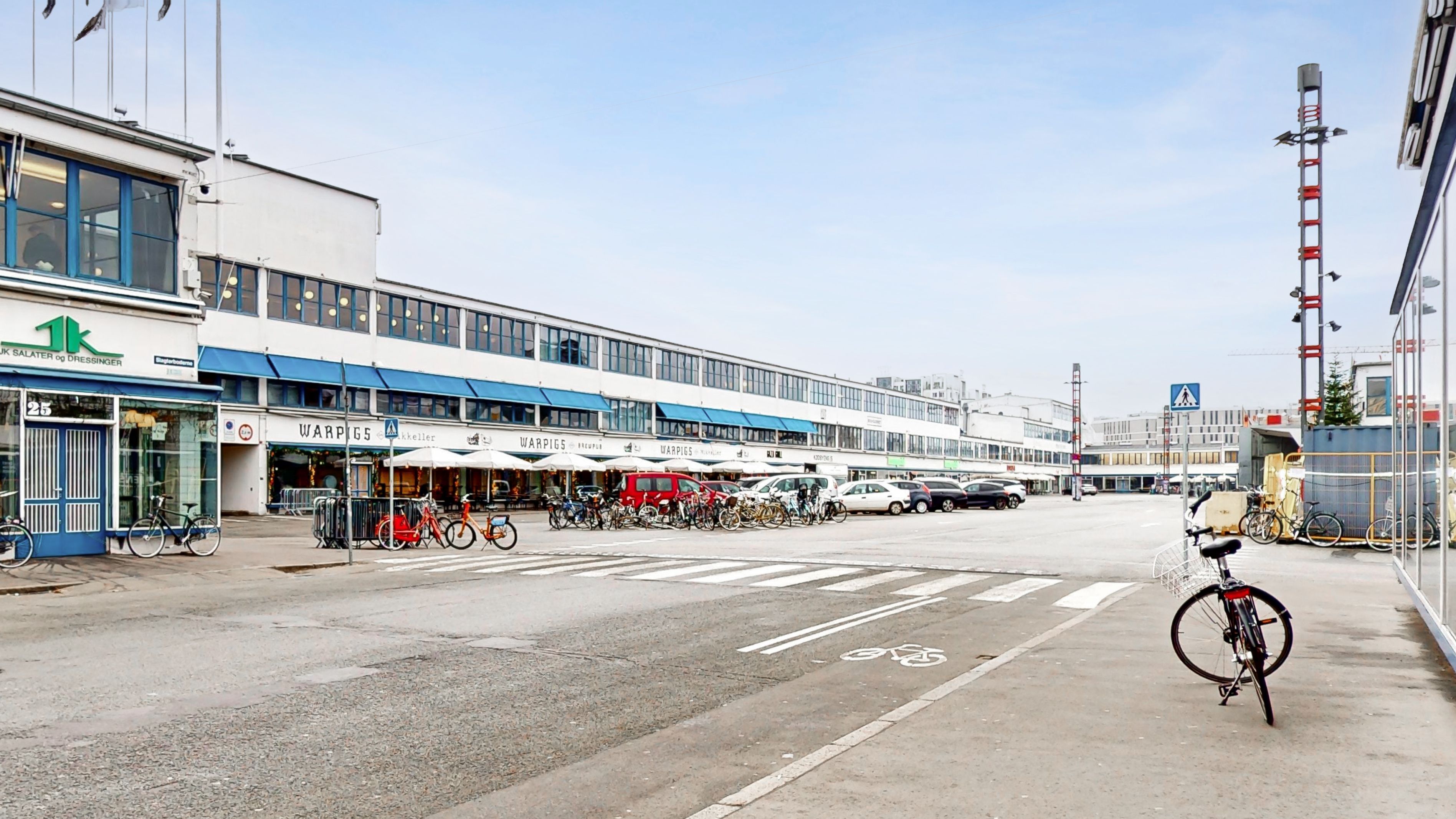 Forretningsbygning med Warpigs og K Salærer & Dressinger, hvor cykler er parkeret og vejkryds med cykelvej og snorpåslag