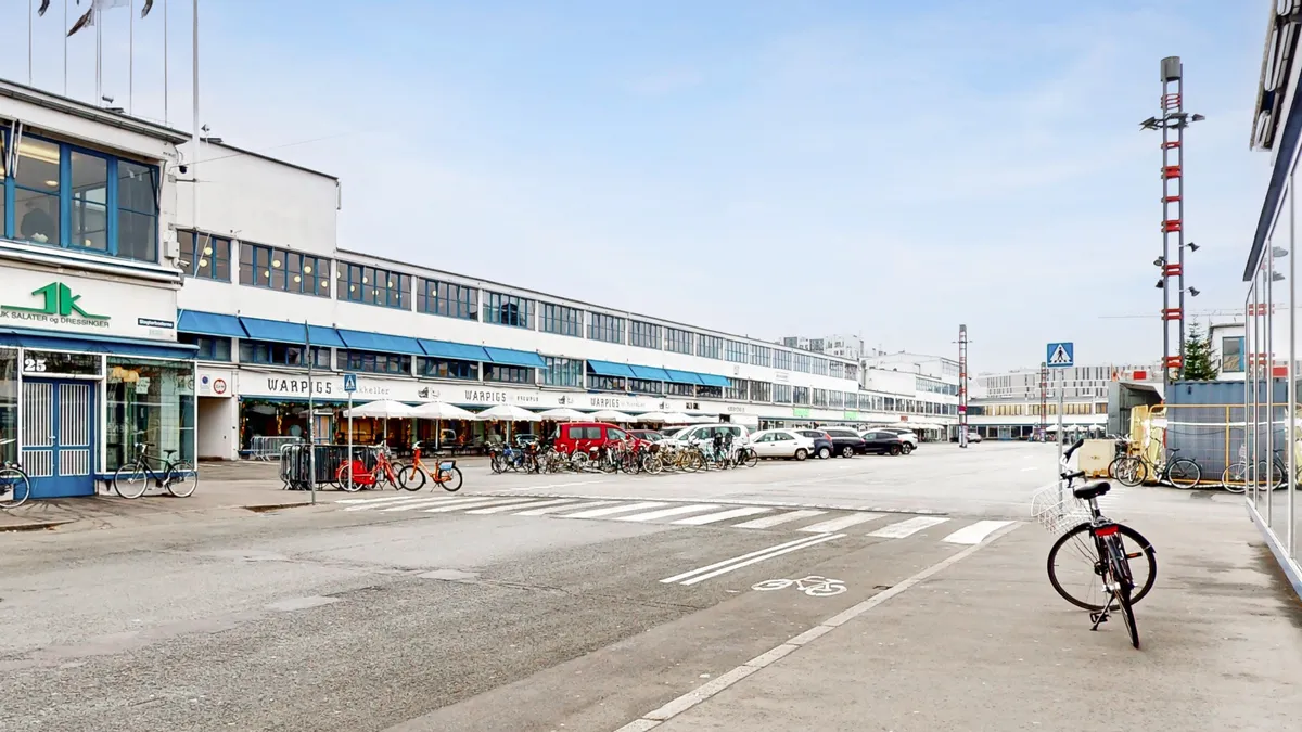Forretningsbygning med Warpigs og K Salærer & Dressinger, hvor cykler er parkeret og vejkryds med cykelvej og snorpåslag