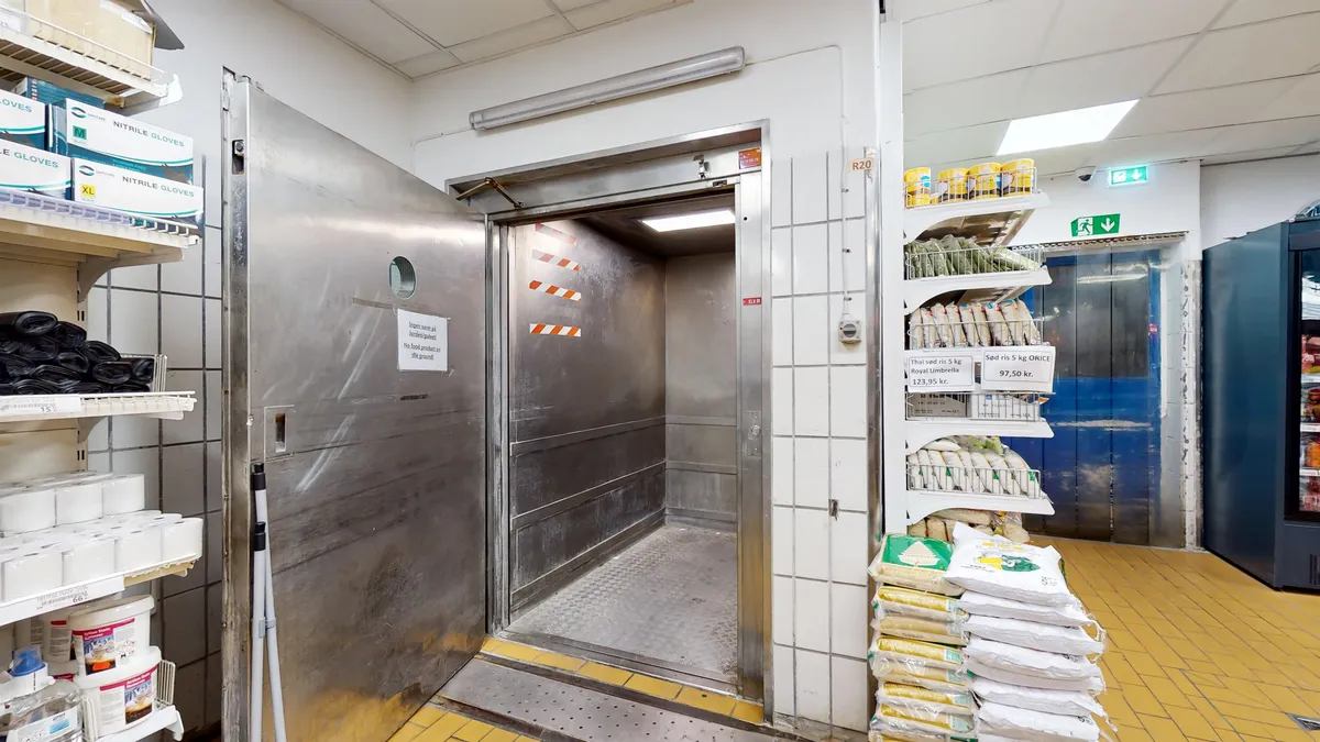 Kødbyens erhvervslejemål med indgangsdør og lagerrum, hvor varer som drikkevarer, frosne produkter og andre varer er placeret på hylder