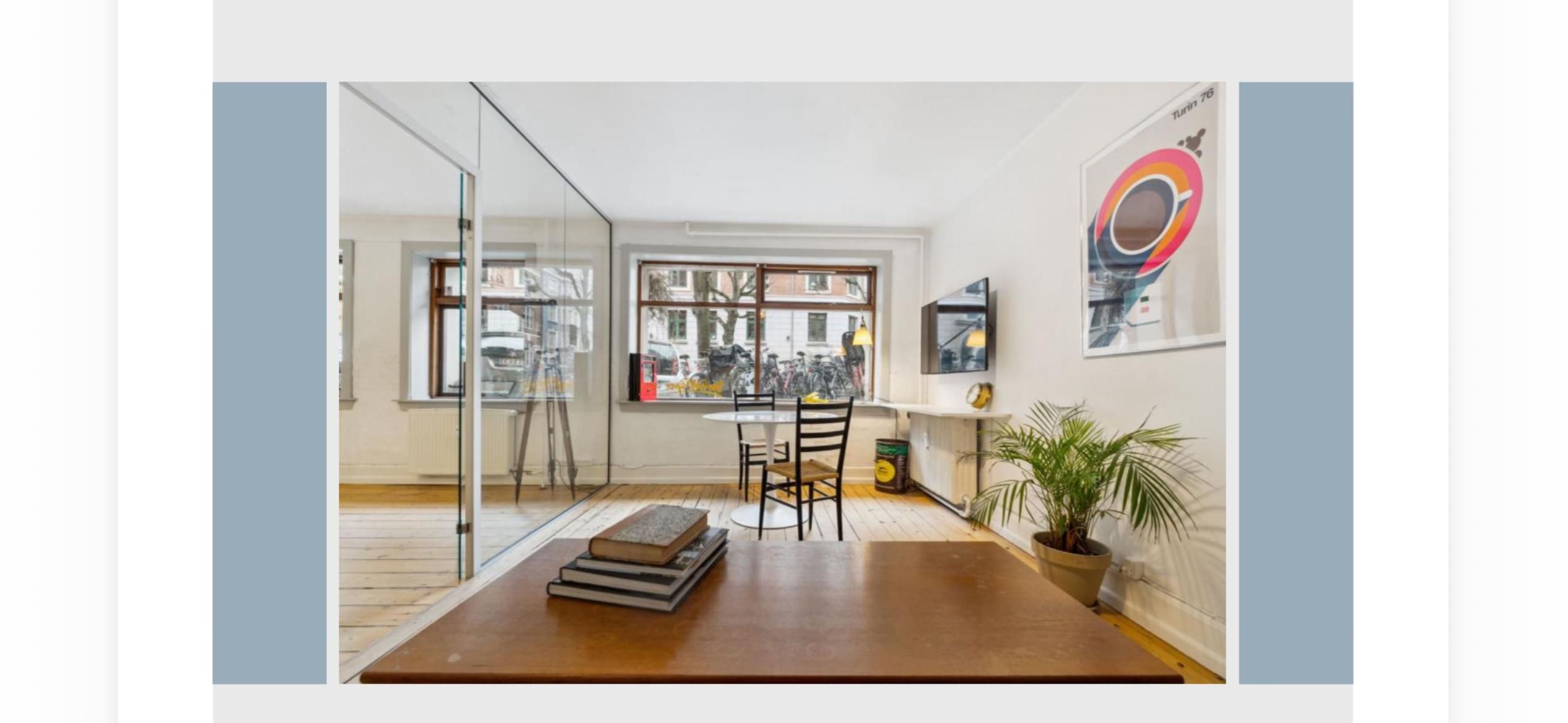 Lokale til leje med moderne møbler og lyse vinduer, et bord med bøger og en terrasse med udsigt til grønne træer