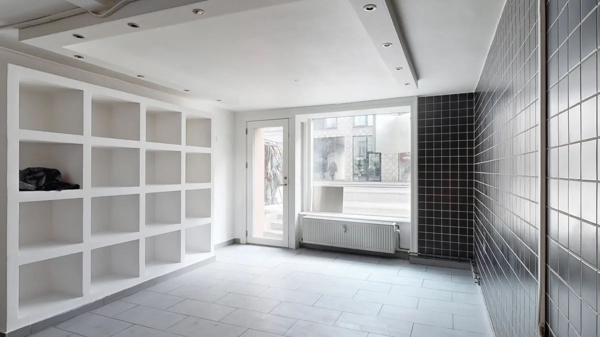 Et nyt, rent og velrenoveret erhvervslejemål med højloft, lyse og lyseglasvinduer, nye radiatorer, hvide hylder og moderne gulvbelægning samt et nyt køkken