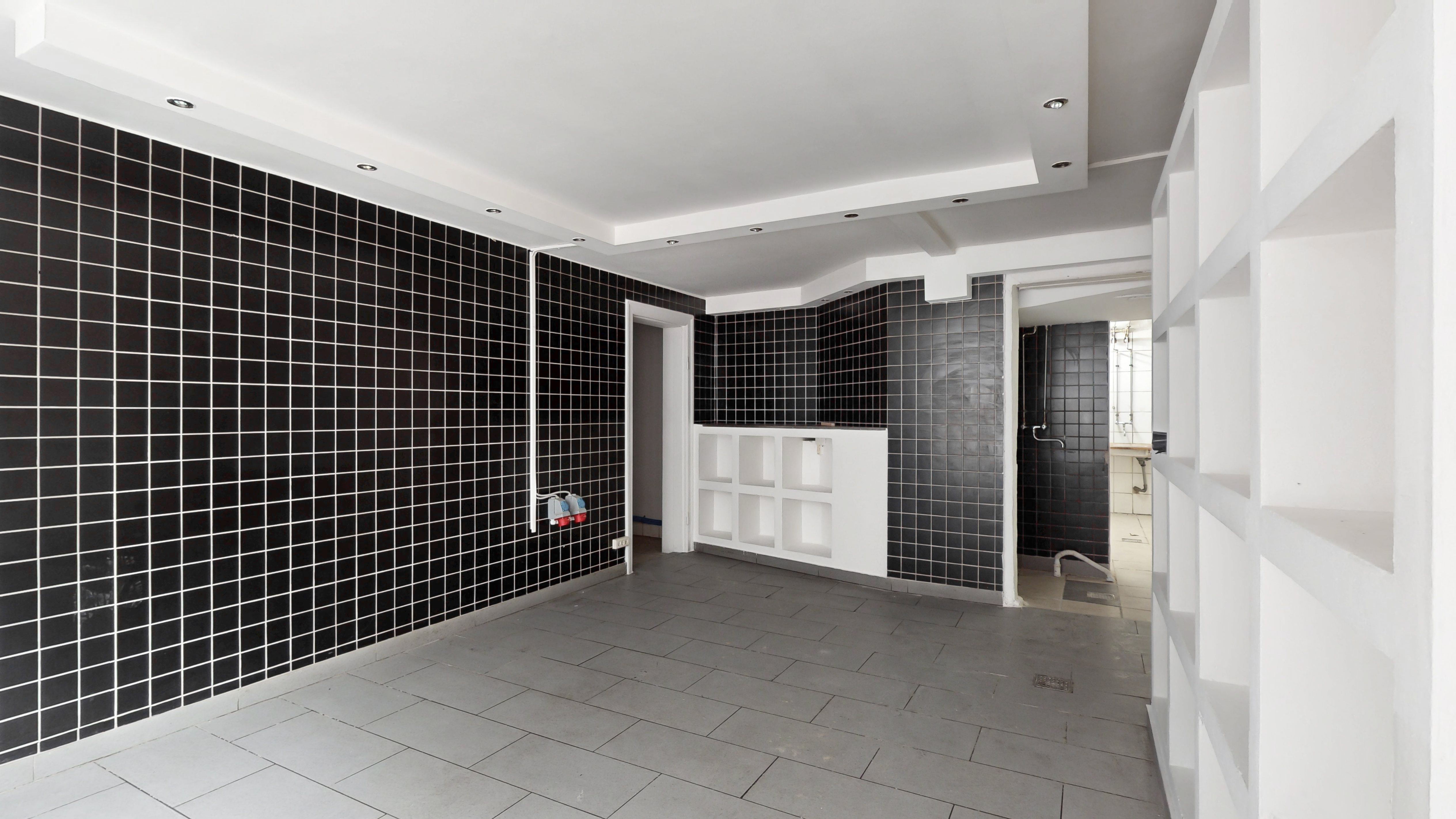 Store værelse med blanke vægge, hvide lofter, sortflisede vægge og højloftede lofter, med lyse, hvide hylder og indgang til et andet rum med badekar og møbler