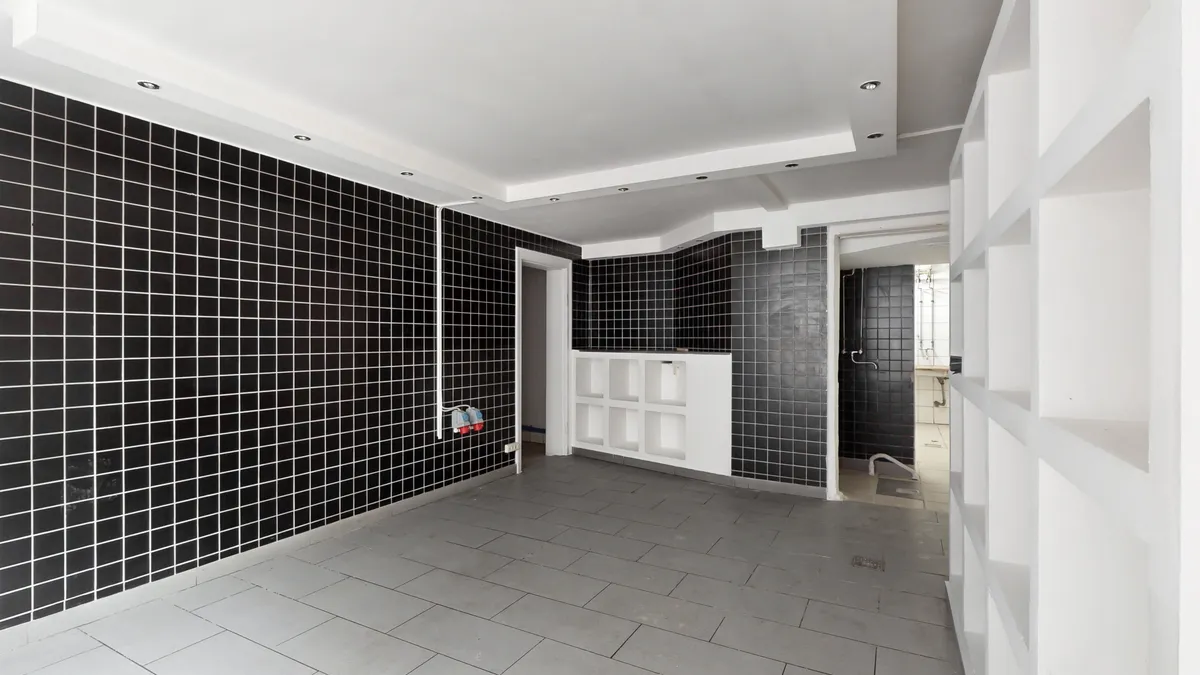 Store værelse med blanke vægge, hvide lofter, sortflisede vægge og højloftede lofter, med lyse, hvide hylder og indgang til et andet rum med badekar og møbler