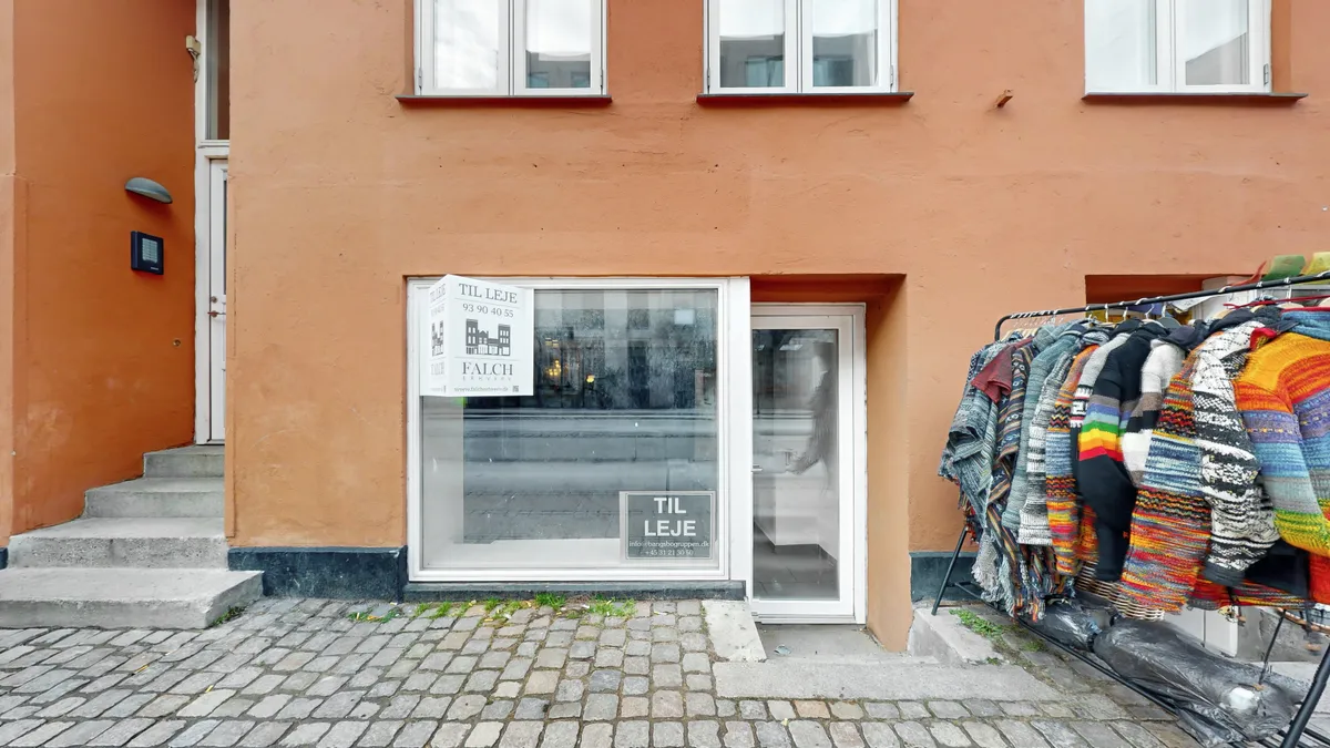 Lejlighedsdør med skilt til leje og hængende tøj på stang med klippesten og trapper i rødt bygning med mange vinduer og søjler