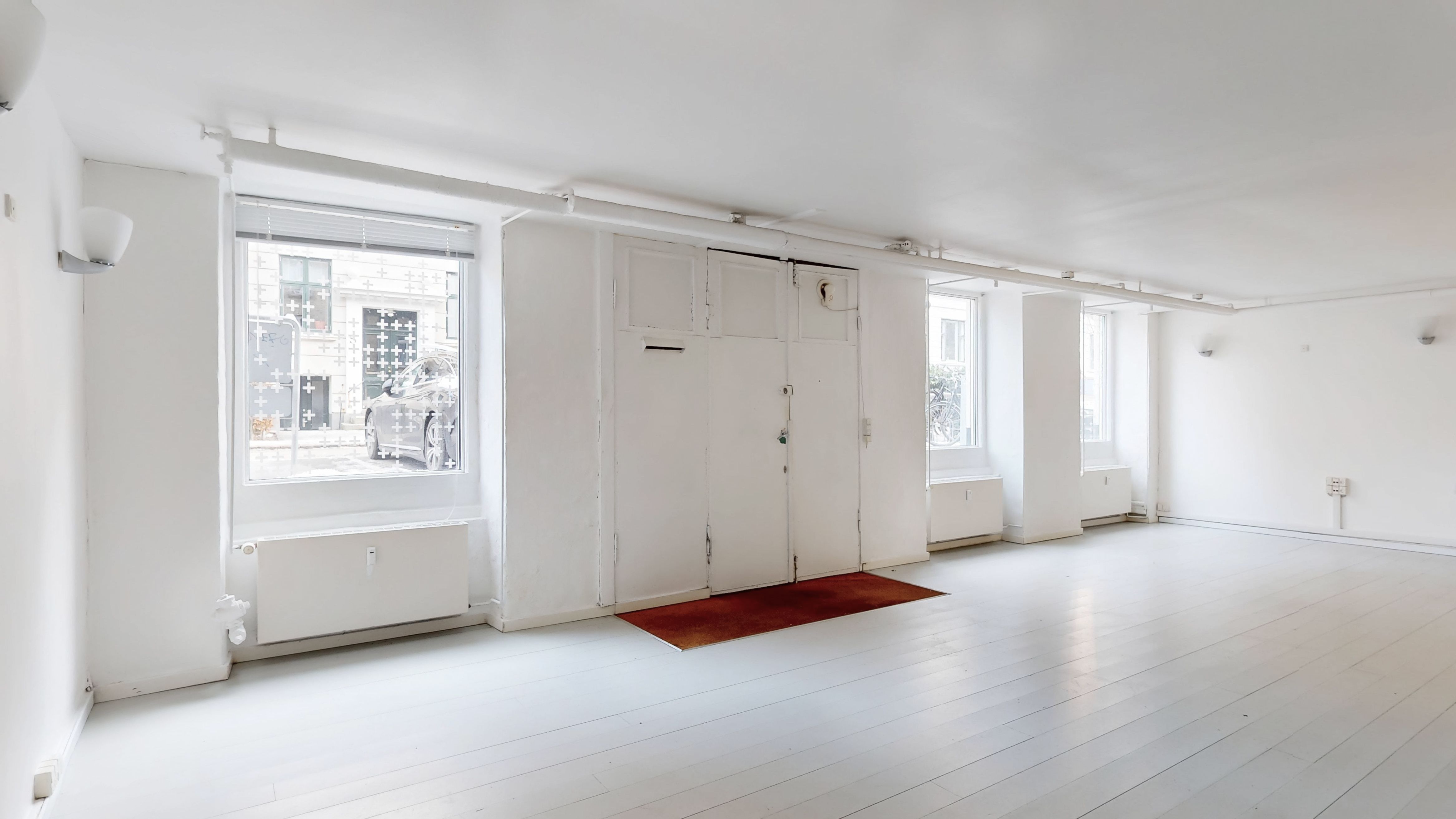 Erhvervslejlighed med lyse værelser og hvide gulve, en stor dør og vinduer, hvorfra man ser en bil og et højhus