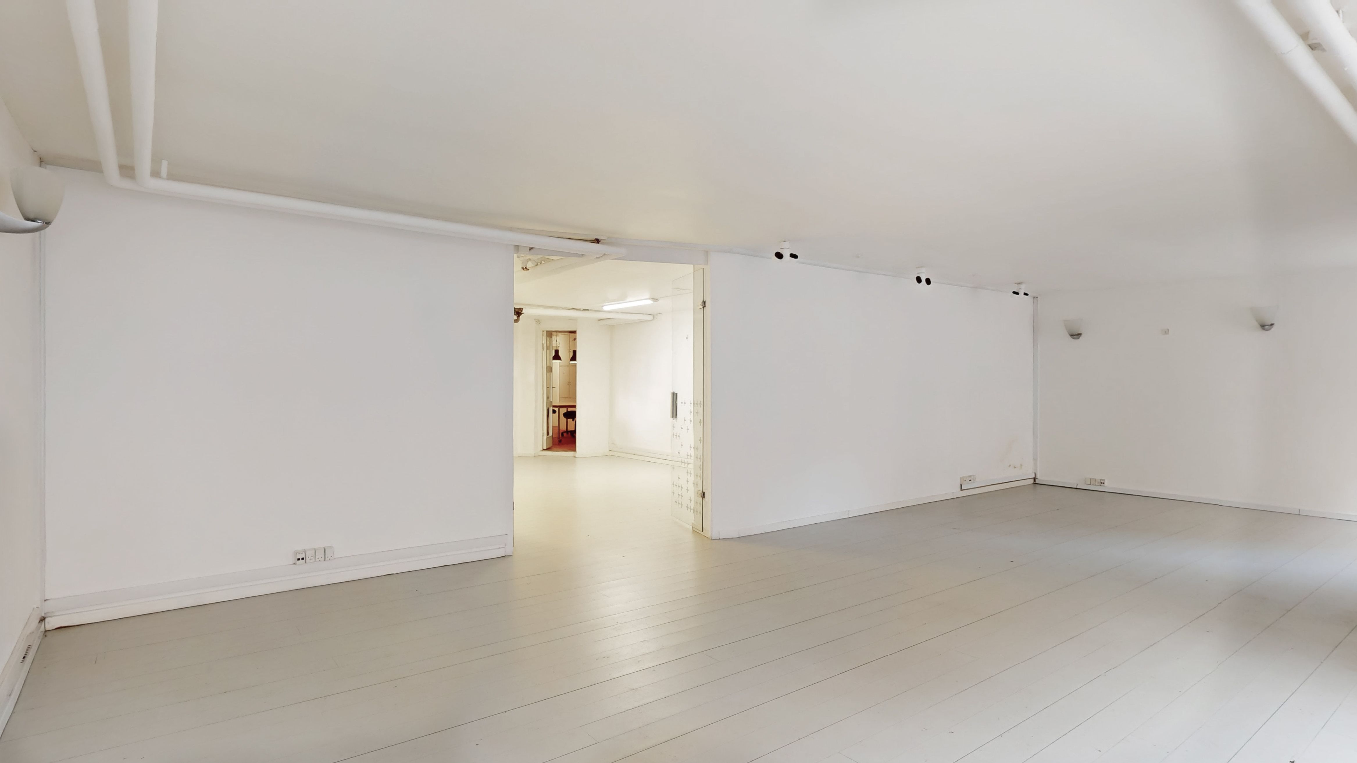 To hvide vægge med loftslamper og indbygget belysning samt åbne døre til rum med møbler og gulvbelægning