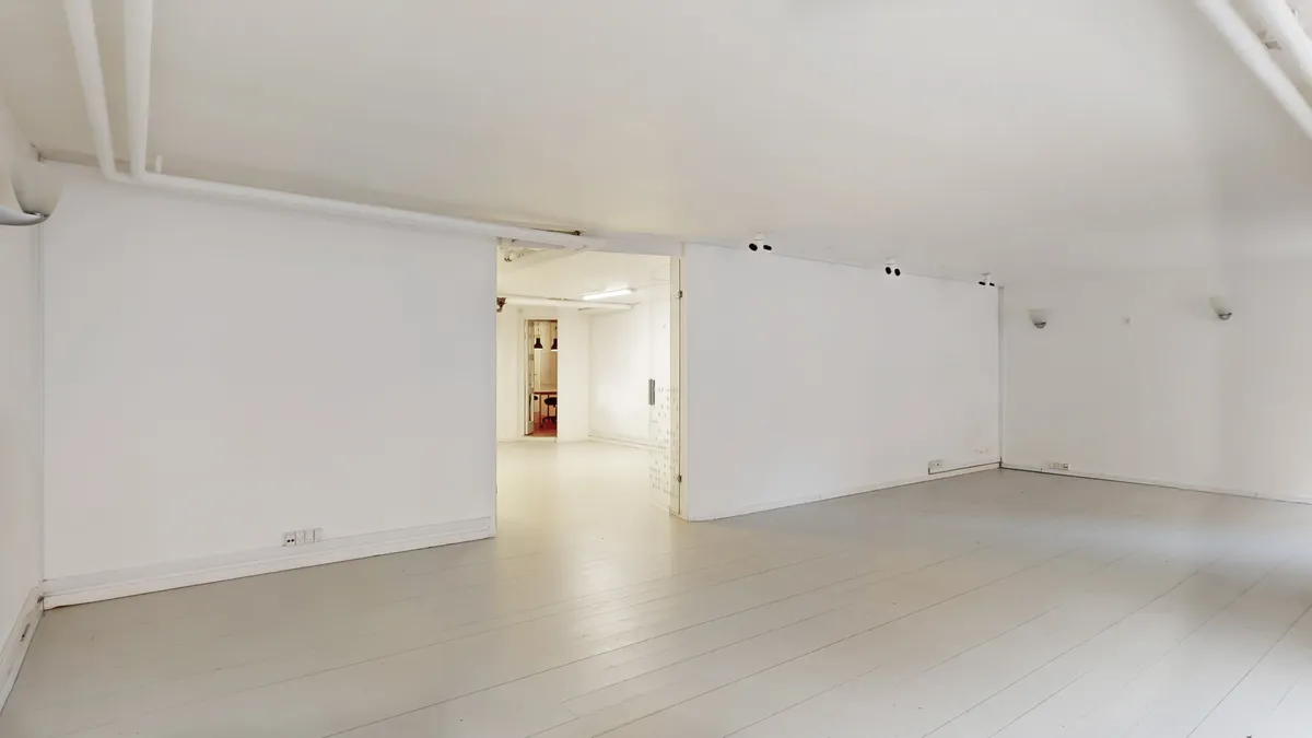 To hvide vægge med loftslamper og indbygget belysning samt åbne døre til rum med møbler og gulvbelægning