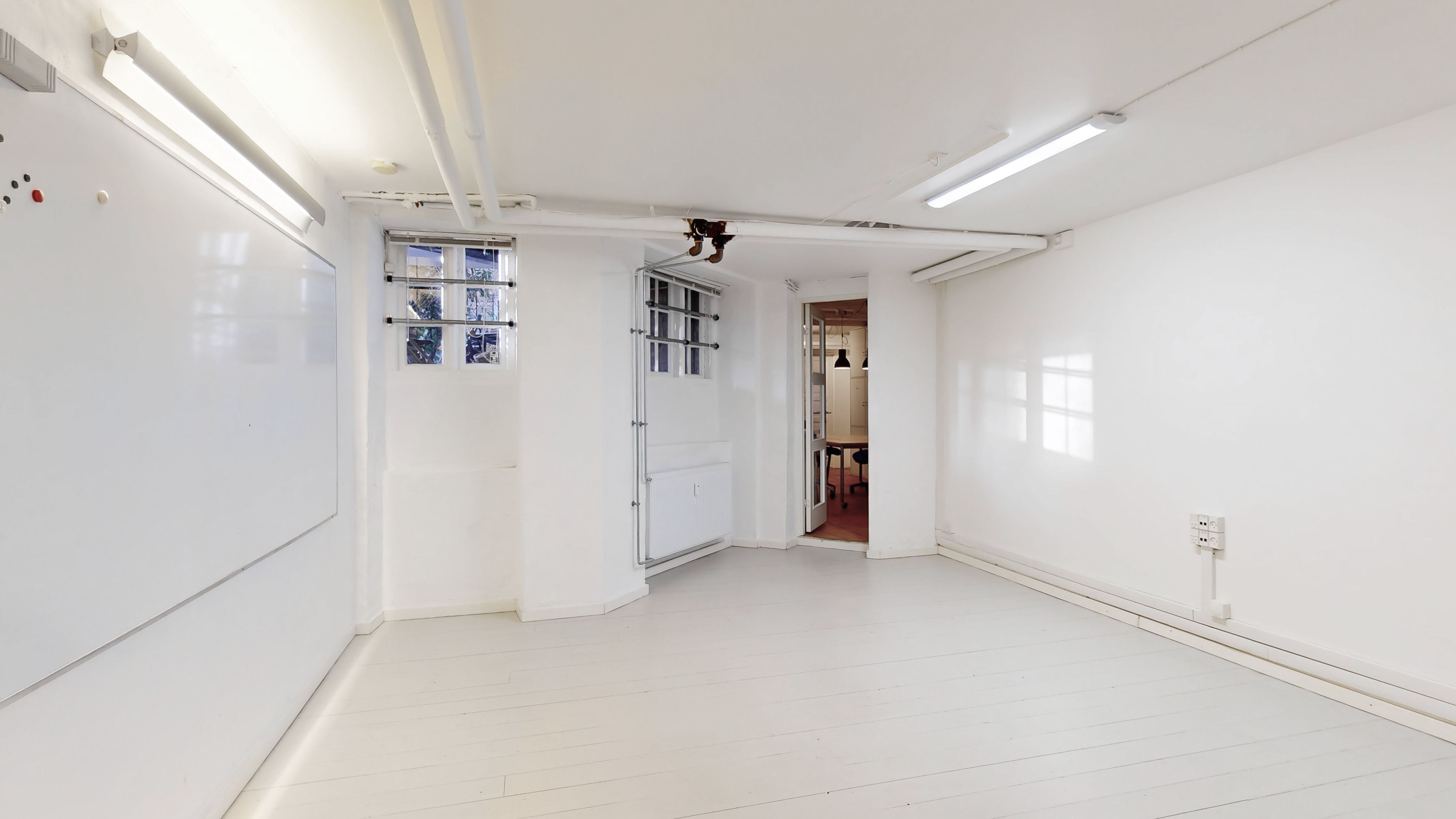 Erhvervslejlighed med to vinduerne, åbne døre og indgangsdør, hvidt gulv og hvide vægge, samt lys på loftet