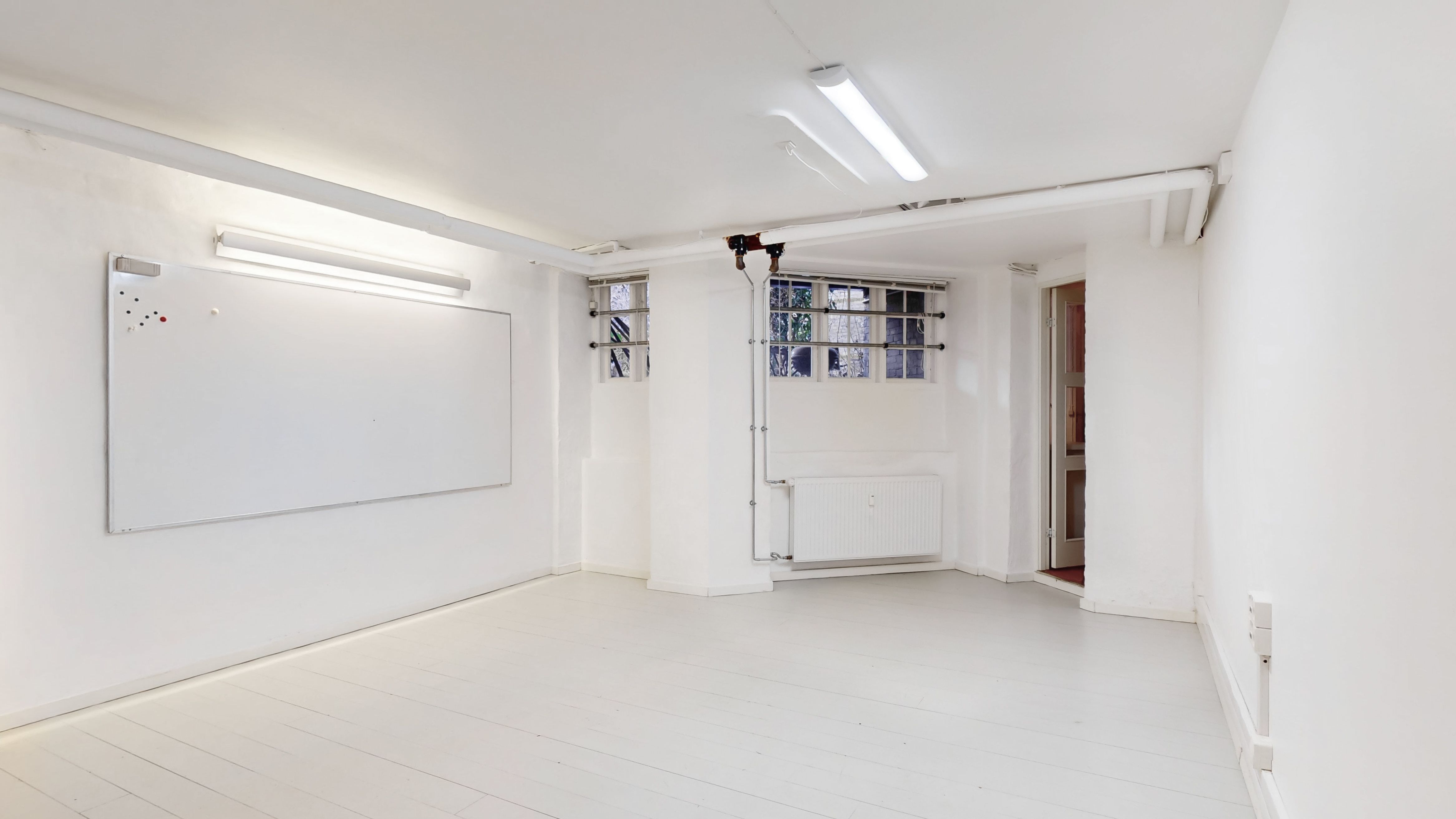 En tom erhvervslejlighed med hvide vægge og gulv, tørre vægge og loft, et hvidt tavlebord og to lysekroner