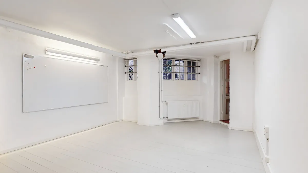 En tom erhvervslejlighed med hvide vægge og gulv, tørre vægge og loft, et hvidt tavlebord og to lysekroner