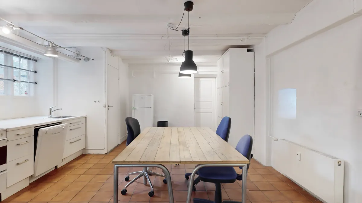 En moderne køkken med et stort træbord og fire lyseblå stole samt en køleskab og et vindue med skyggegardiner