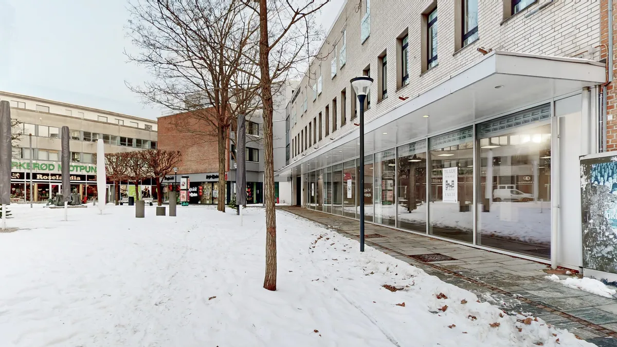 Et snebelagt gadestykke med et særdeles rummeligt erhvervslejemål, et højt bygningshus med glasvinduer og et søjlelys langs fortovet