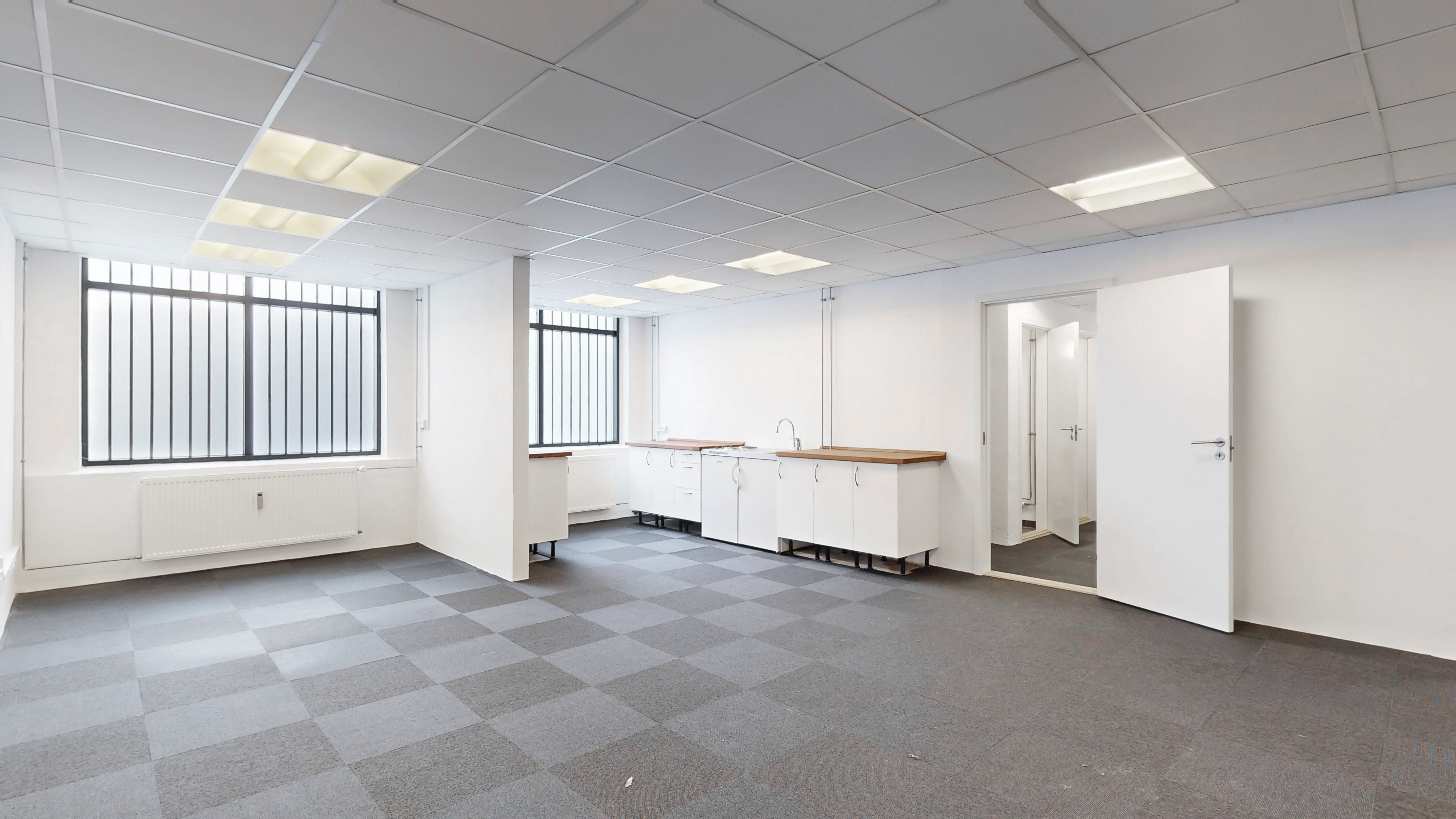 Store kontorlokaler med hvide vægge, lyskryds, moderne køkken med hætte over ovnen og store vinduer med ruder.