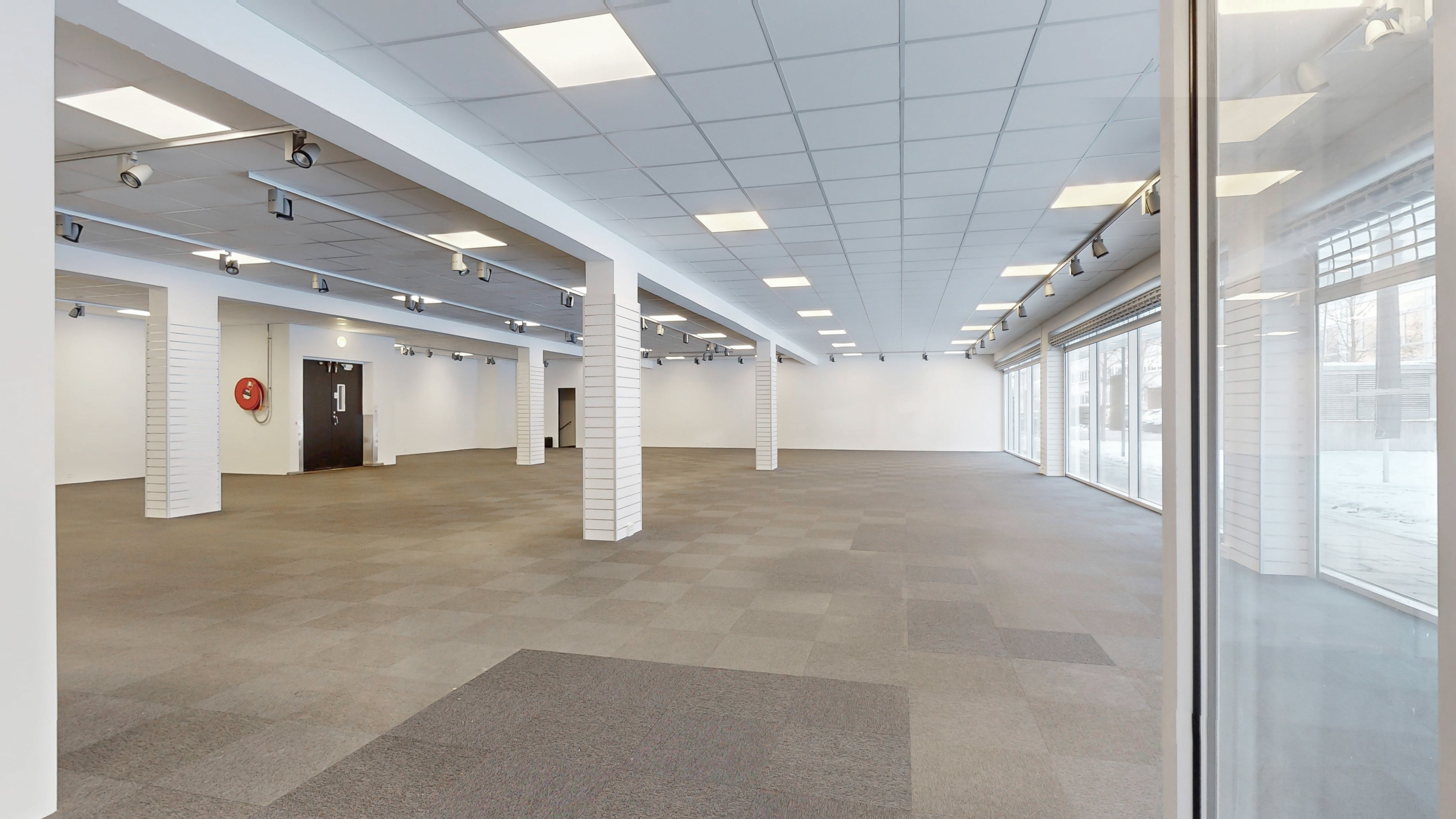 Et tomt erhvervslokal med højt til loftet og lyse loftsbælge. Store glasruder og tavlepaneler giver godt lys. Store døre og gulve med kvadratiske mønstre