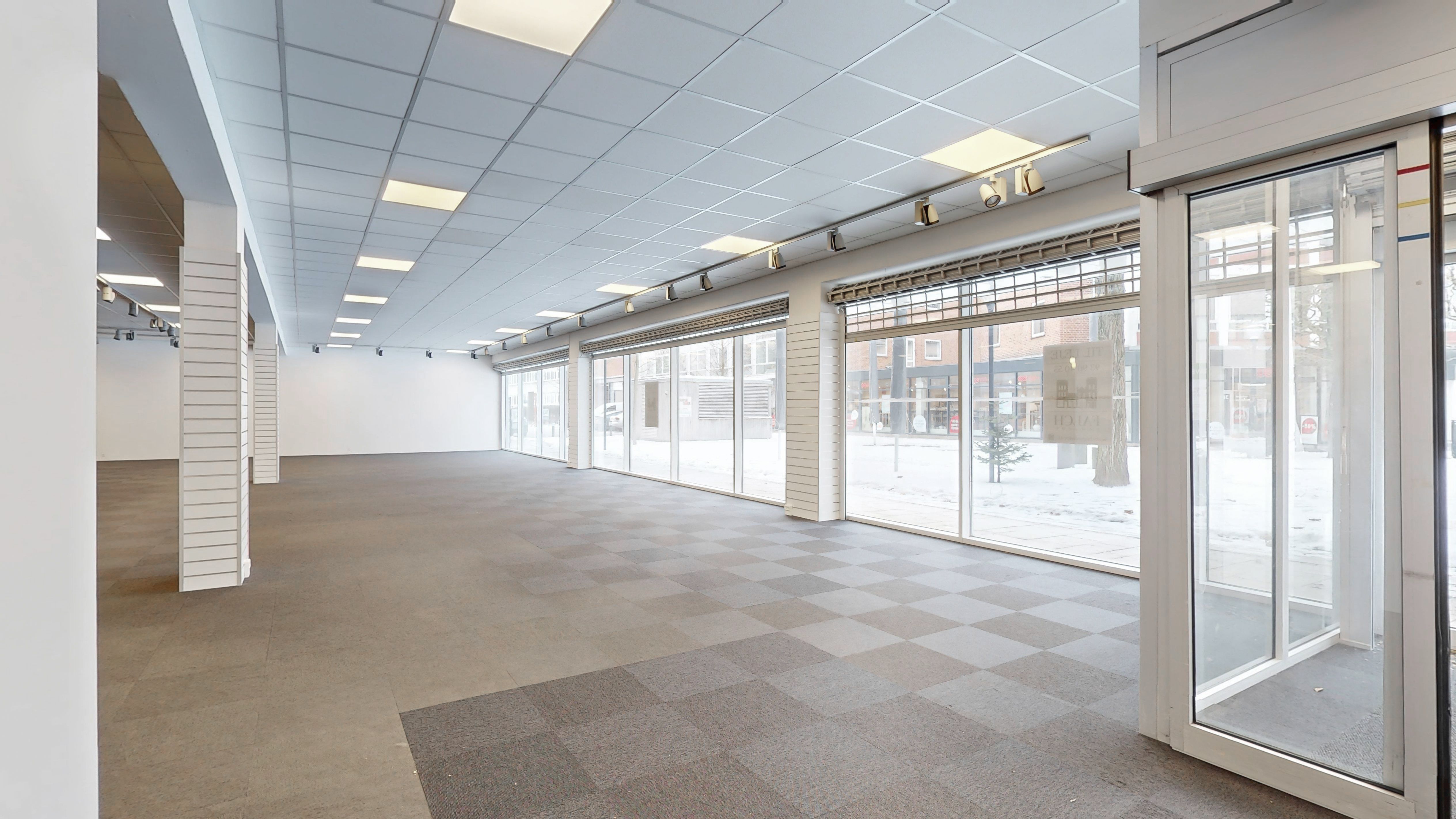 En stor, tom erhvervsejendom med tavler på væggen, en stor indgangsdør, glasruder og en lys gulvbelægning
