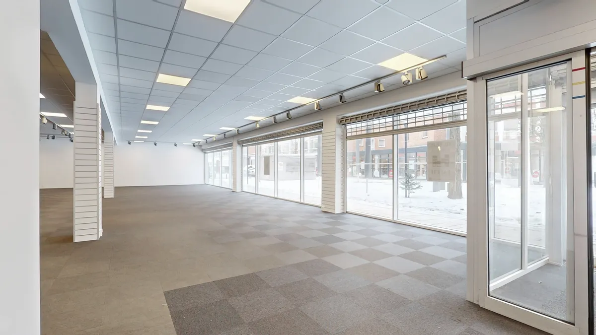 En stor, tom erhvervsejendom med tavler på væggen, en stor indgangsdør, glasruder og en lys gulvbelægning