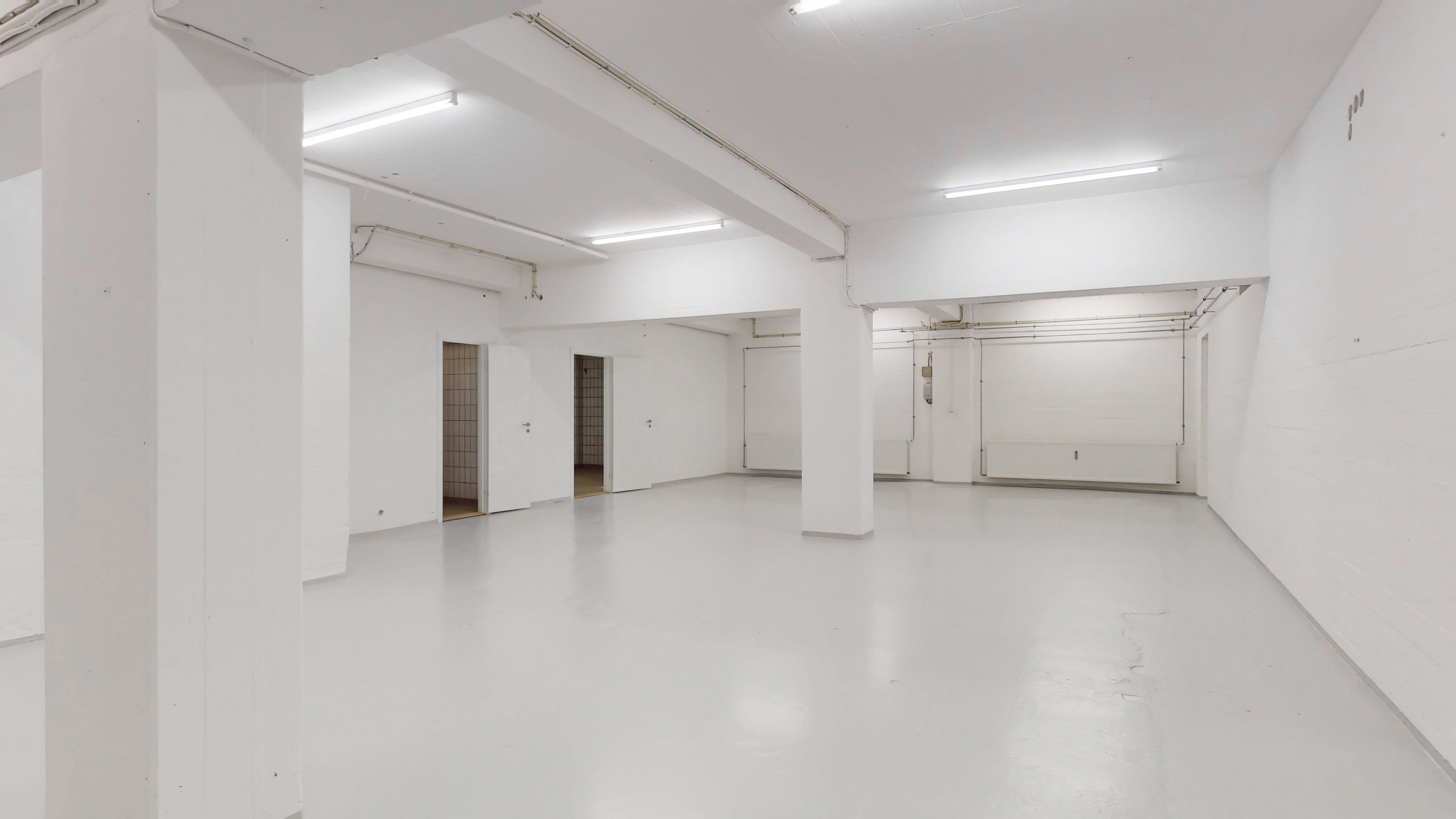 Store lyse lokaler med hvidt gulv og vægge samt åbne døre til mindre rum og radiatorer. Der er fire lysekroner og to ventiler på loftet