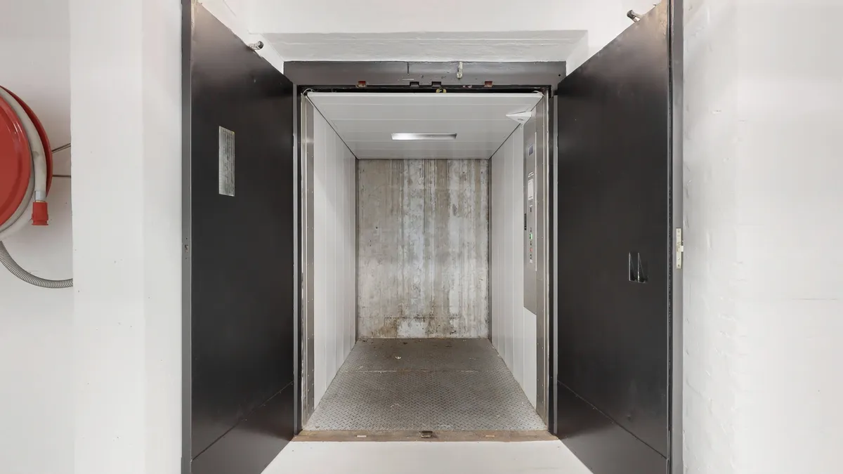 En tom elevator med glas og metal døre, der er åbne med en lys plade og gulvet i elevatoren er af metal.