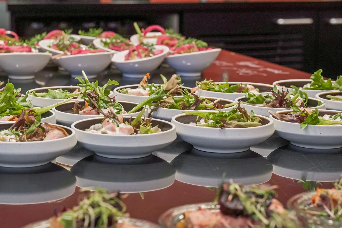 Restaurantbord med små skåle og forskellige grøntsager og salater til buffet. Smagfuld og sund mad med friske grøntsager og salater i små skåle på restaurantbord.
