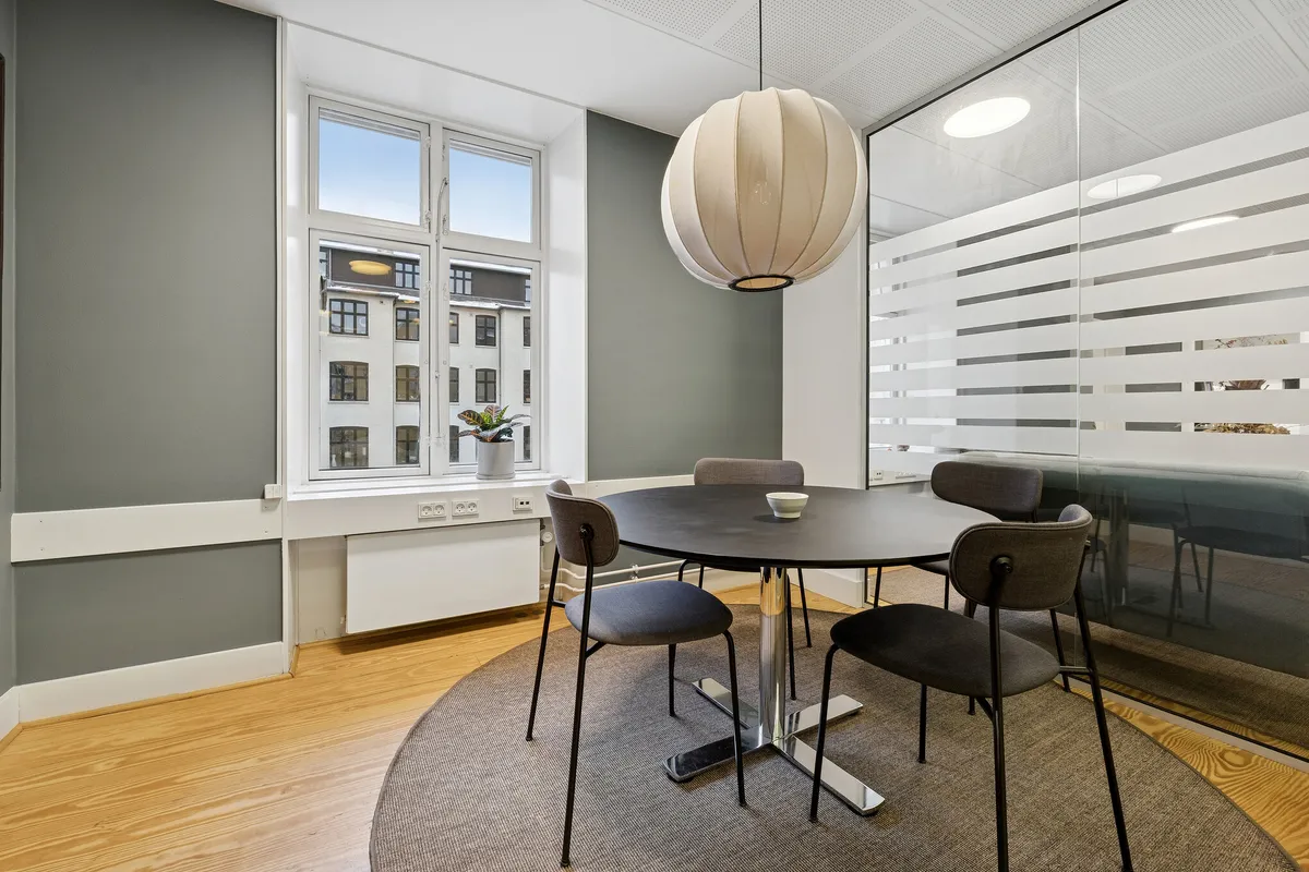 Kontorrum med rundt bord og moderne møbler i en lys og velholdt indretning med store vinduer og lyse lofter