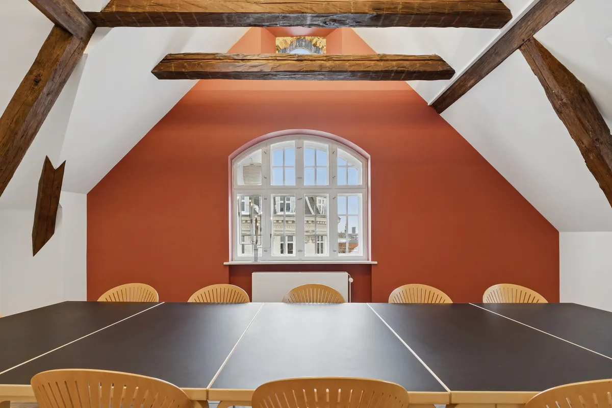 Kontorlokaler med lyse trælofter og røde vægge, slanke vinduer og lyse møbler samt bord og stole i et fredeligt miljø