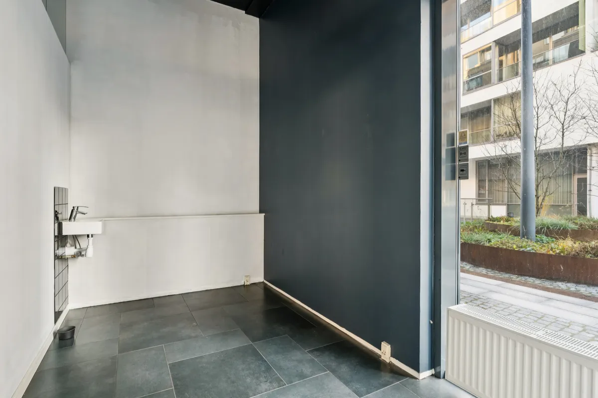 Lej en butik med sort og hvid farvesammensætning og gulvbelægning, synligt udvendigt med planter og bygning i baggrunden.