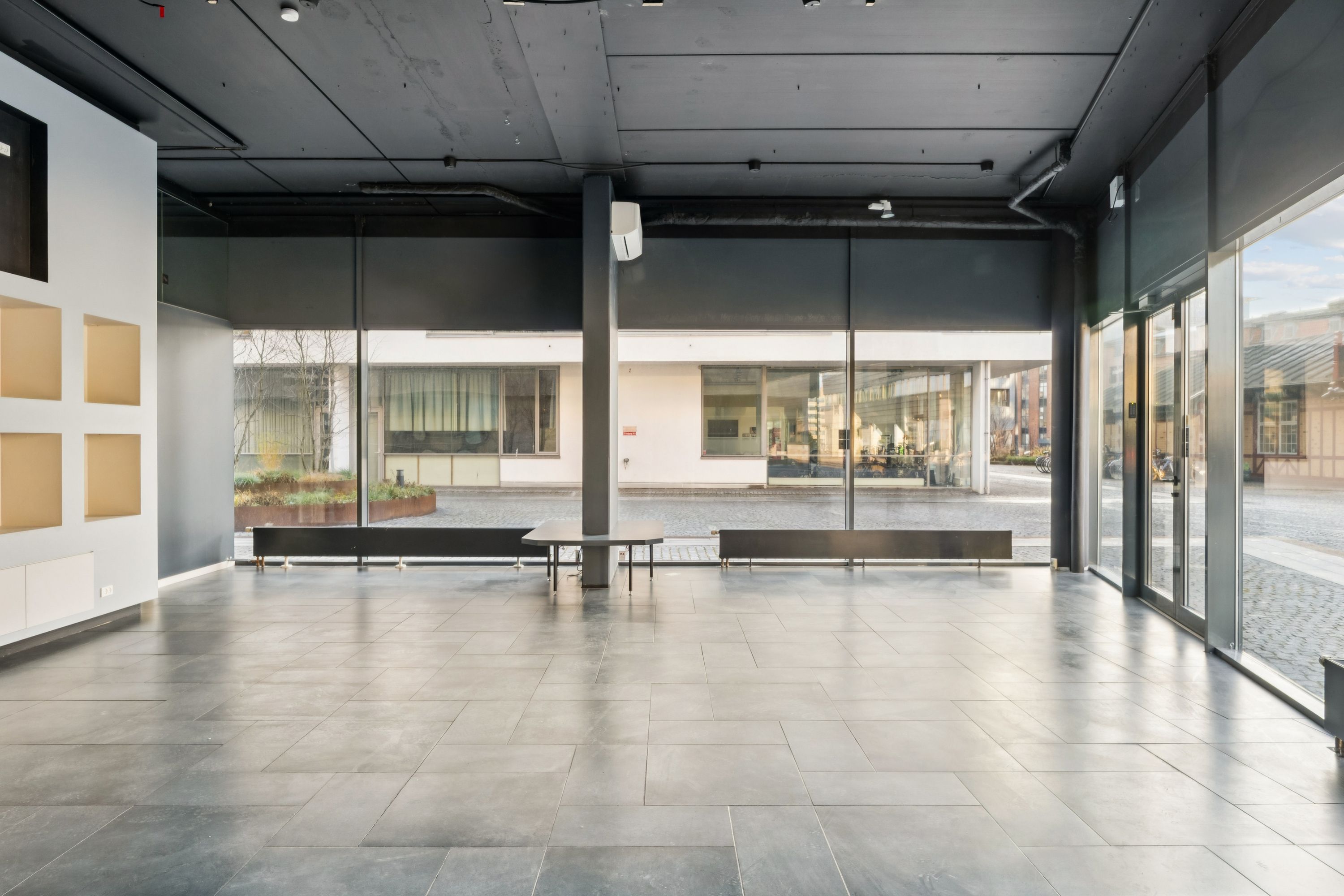 Store glasvinduer og en stor åben indgang i et showroom med tømrerede gulv og smukke hjørnebanke i sort