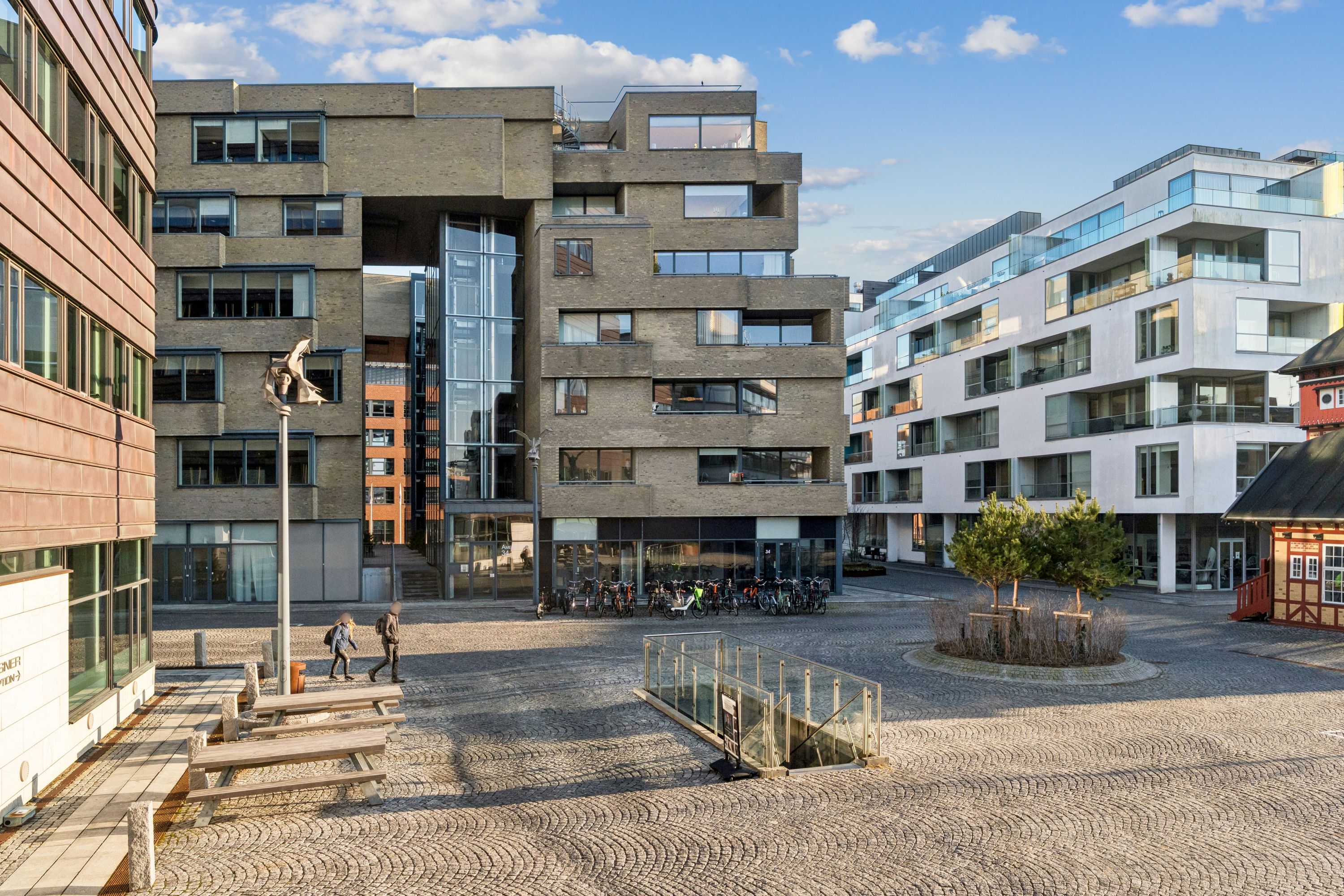 Store glasvinduer og et moderne design er synlige på bygningen på Amerika Plads 34 i København. To personer går uden for butikken og der er flere cykler parkeret.