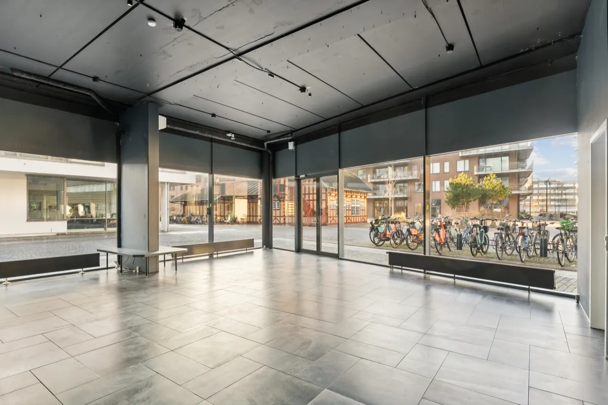 Tommen indgangshal til lejlighed med store vinduer og lysegulv. Udenfor står mange cykler parkeret på cykelstativer og bygninger i baggrunden