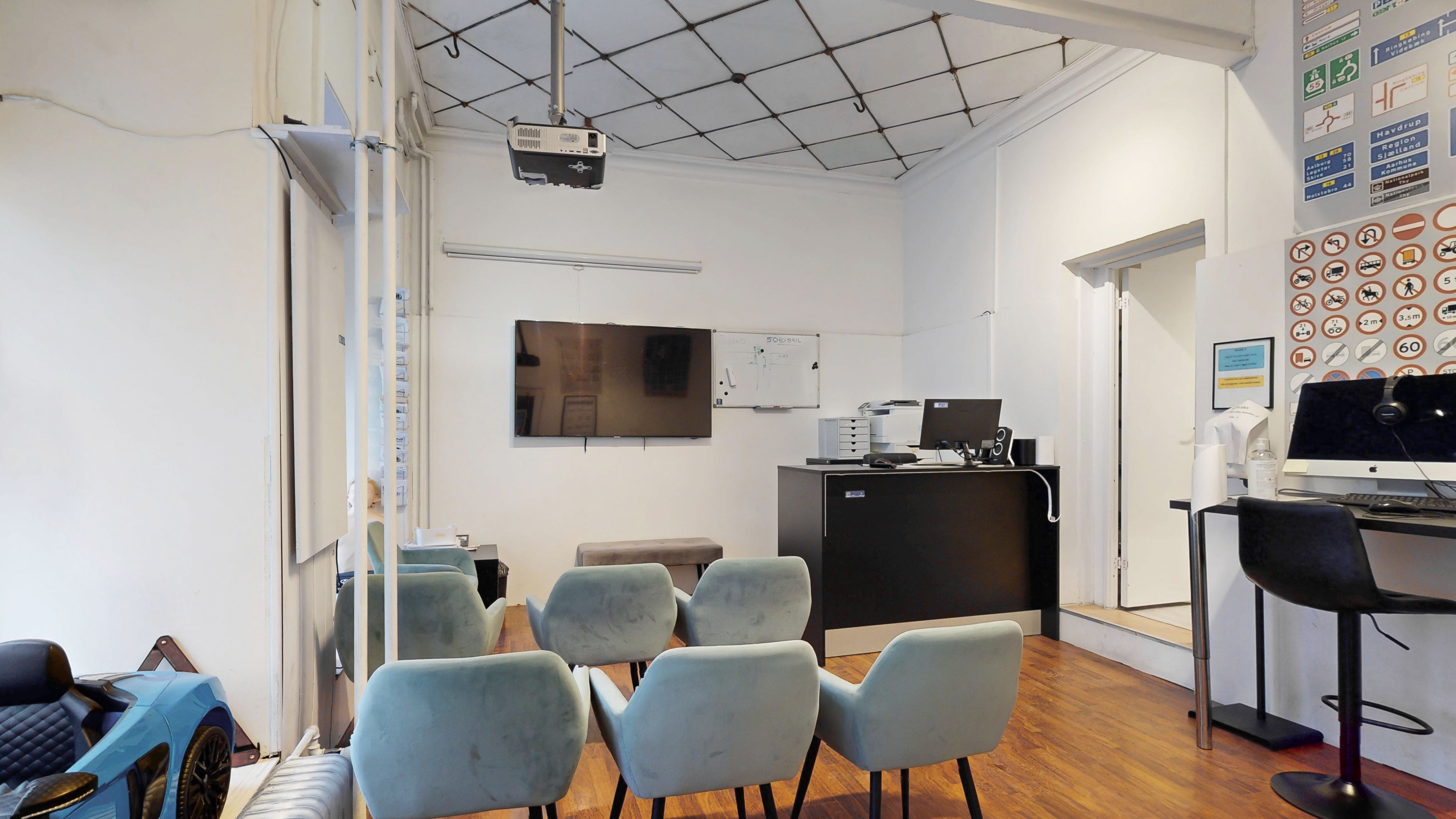 Kontor med skrivebord, højtalere, computer, monitor, tv, stol og sofa i et lyse og moderne kontor.