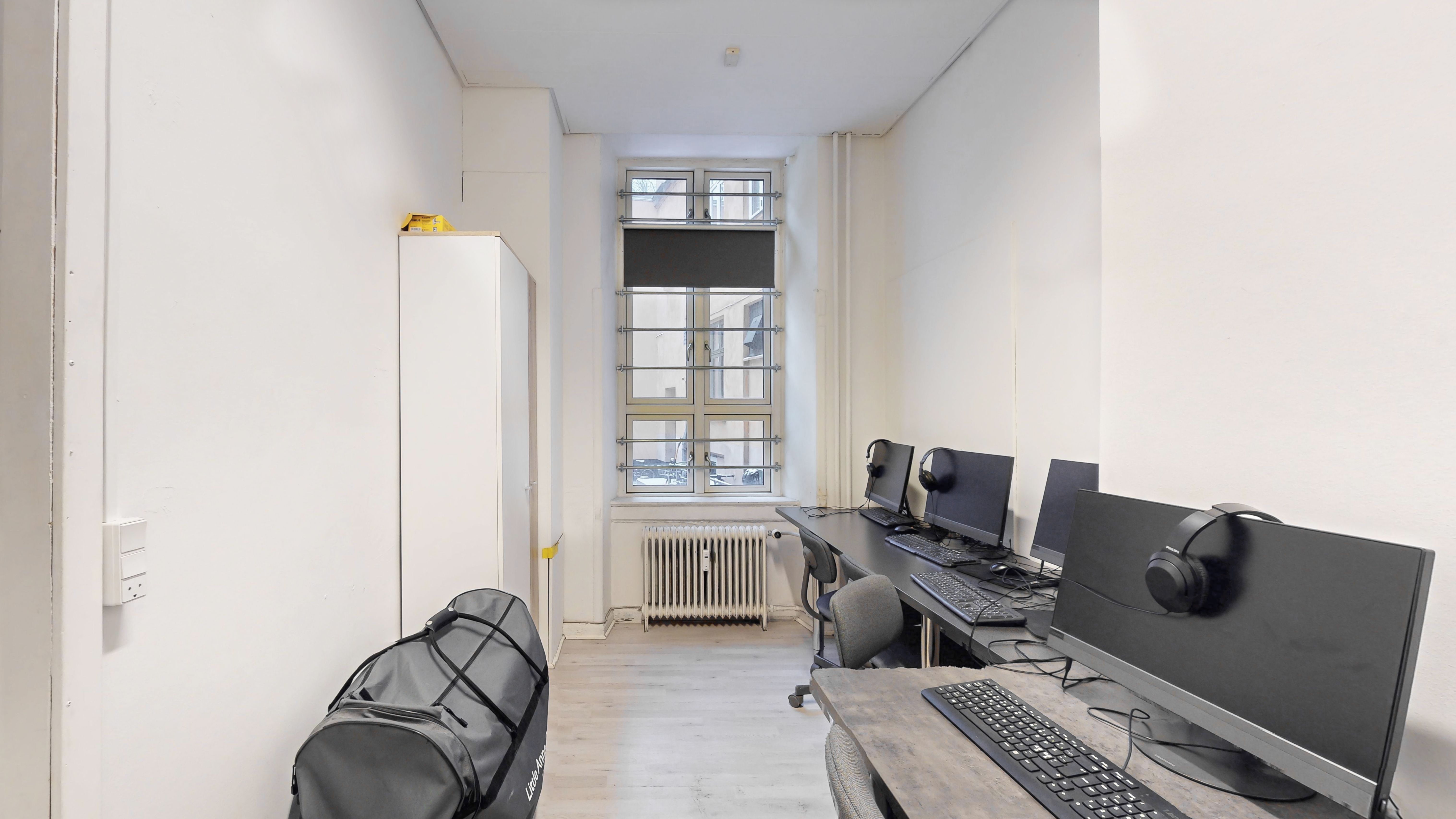 Et kontorlokale med tre computere og deres tilhørende skærme, tastature og mus samt hovedtelefoner placeret på et bord