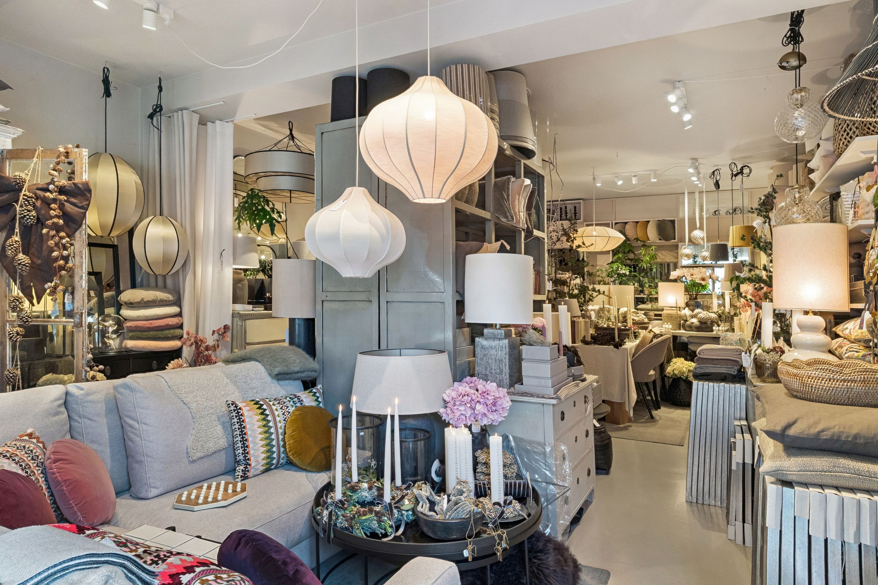 Interiør med sofaer og stole, hvide og grå farver, små hvide lysekroner, lyse og puder, gulve og vægge, hyggeligt og klassisk design, indretning, møbler og tekstiler, hjem.