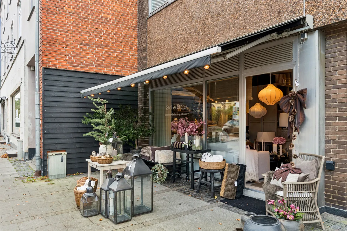 Et elegant møbelforretning med udsmykning i indgangsområdet og lysekroner indendørs, lyse lanterner og plantepoteter udenfor. Lyserøde og gule lanterner og en krans af fyrretræer i indgangsområdet