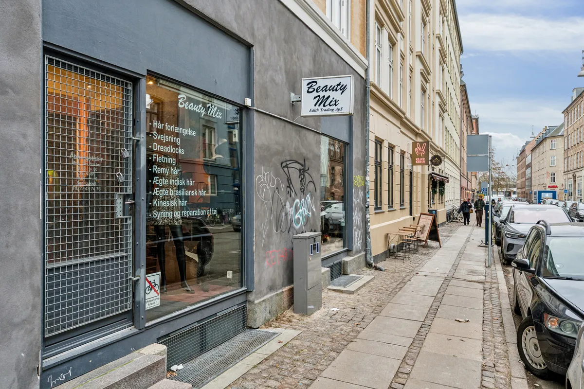 En Beauty Mix butik med et skilt over indgangen og en række tjenester som svejsning og kinesisk. En række biler er parkeret på siden af gågaden.