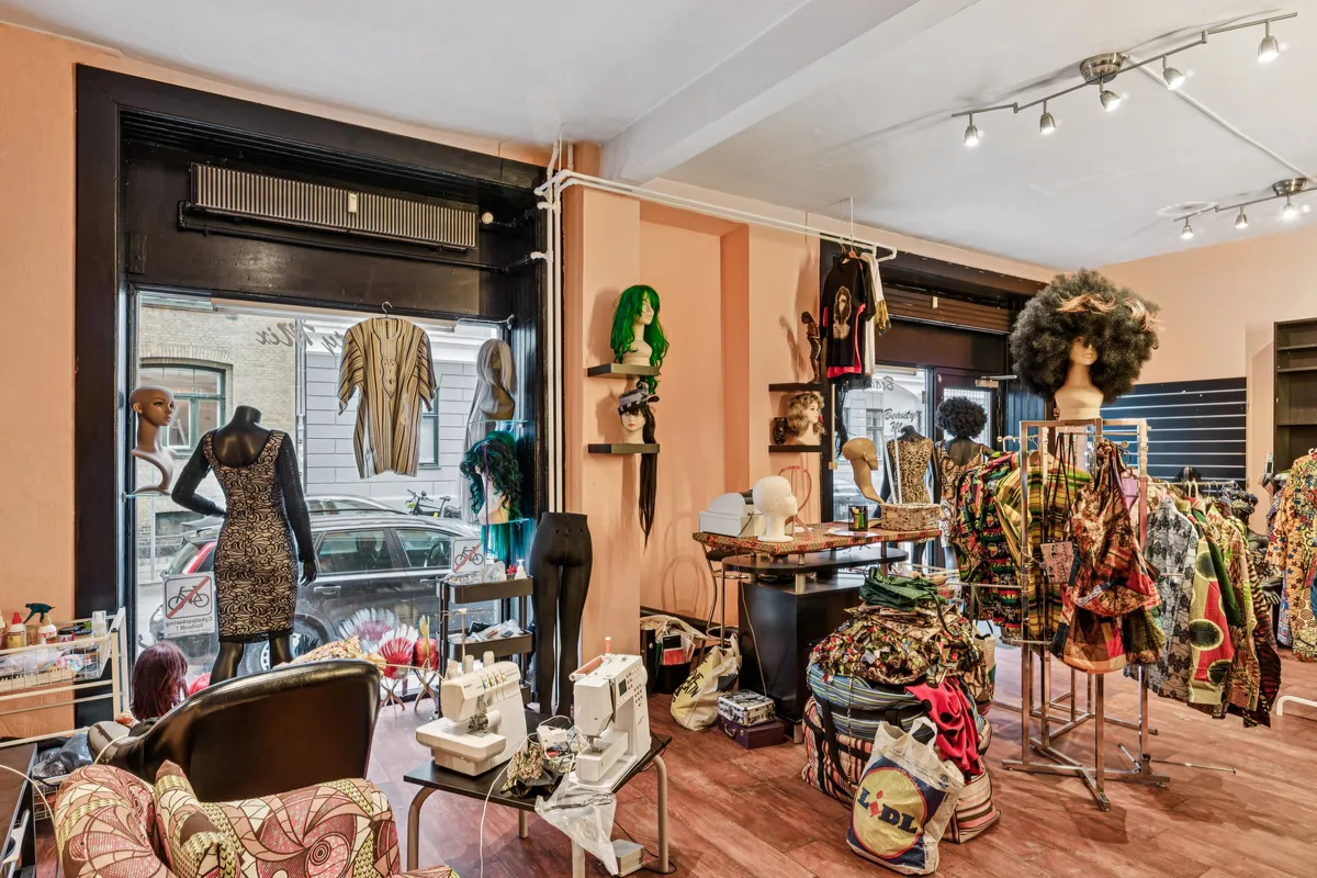 Københavnsk butik med mange tøjstykker, mønstre og manequins. To symaskiner og stole i forgrunden. Glasskure med biler og bygninger bagved